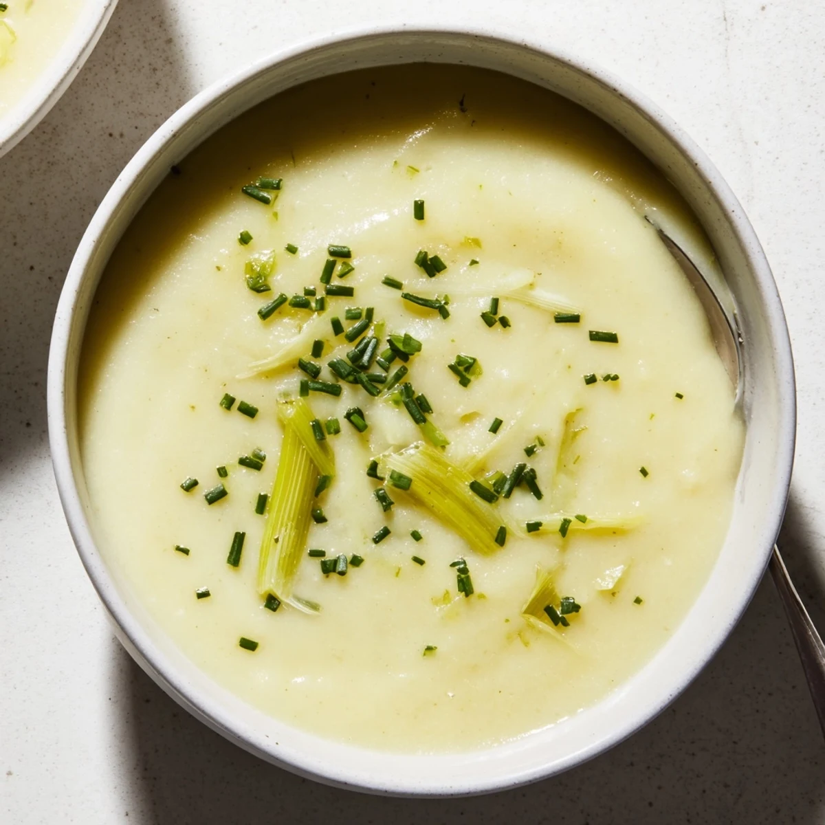 A bowl of creamy leek and potato soup, garnished with chives, ready to eat.