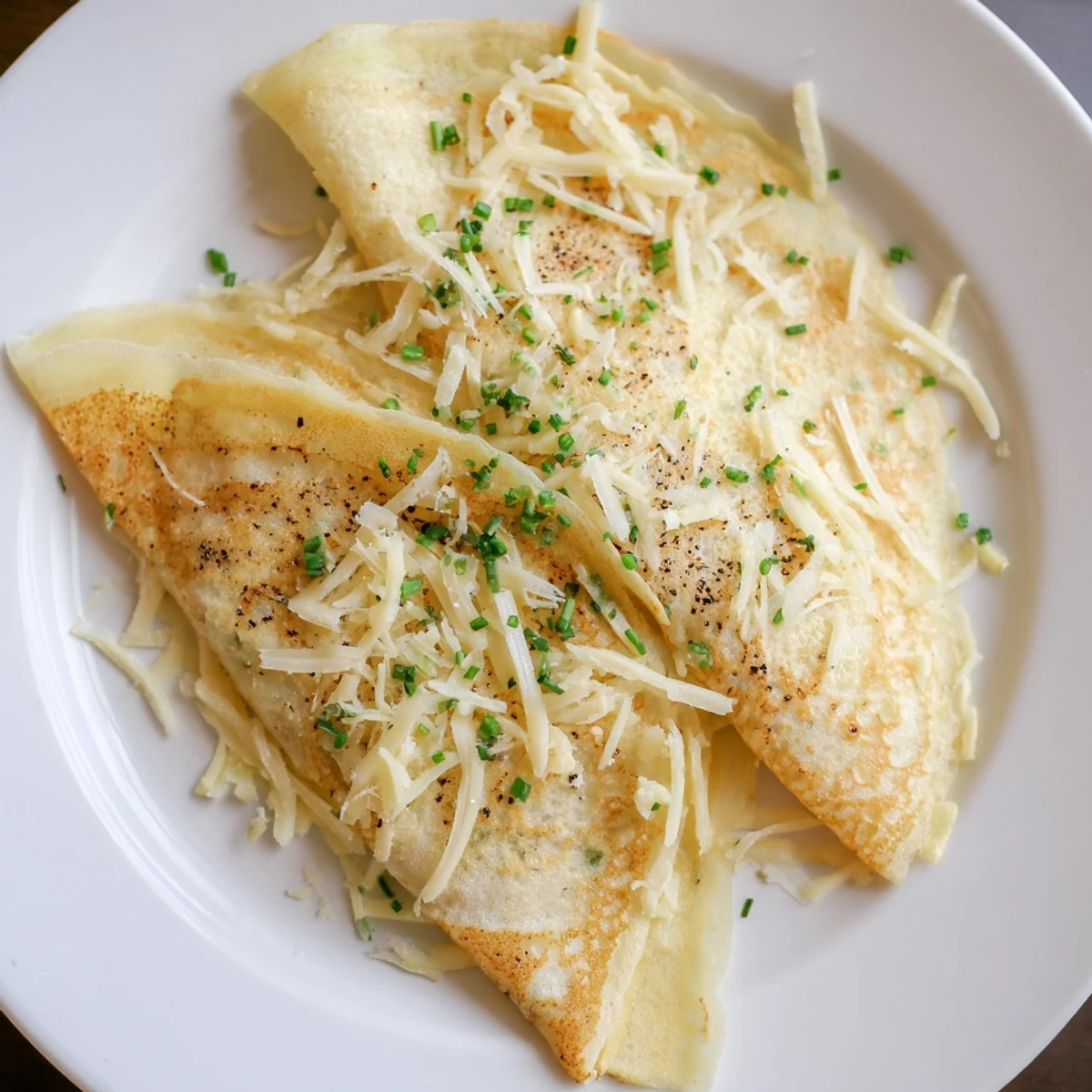 Golden-brown Savory Crepe with Cheese folded into quarters, oozing melted Gruyère and mozzarella on a rustic wooden plate.