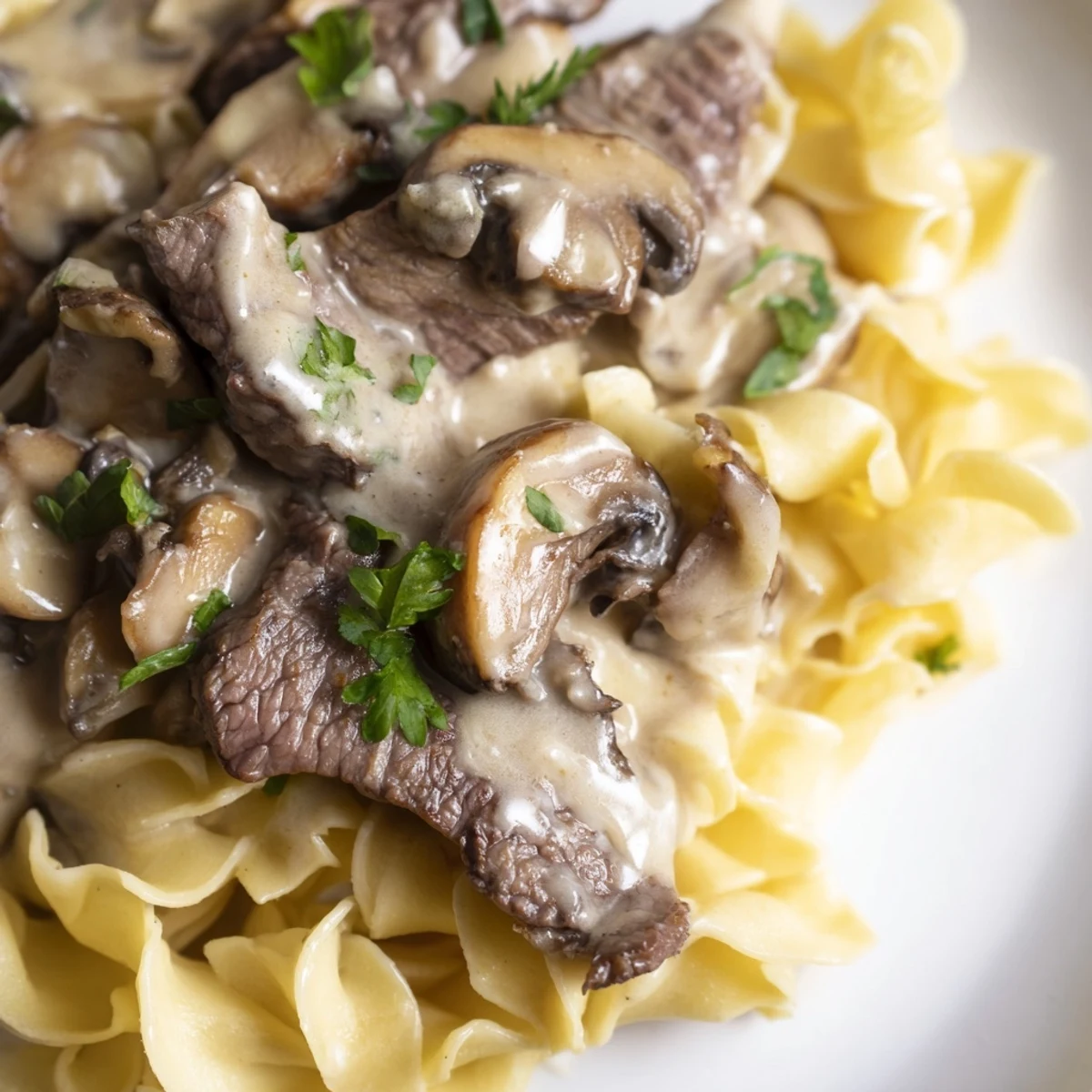 Steaming beef stroganoff over a mound of wide egg noodles, garnished with fresh parsley for a classic family dinner.