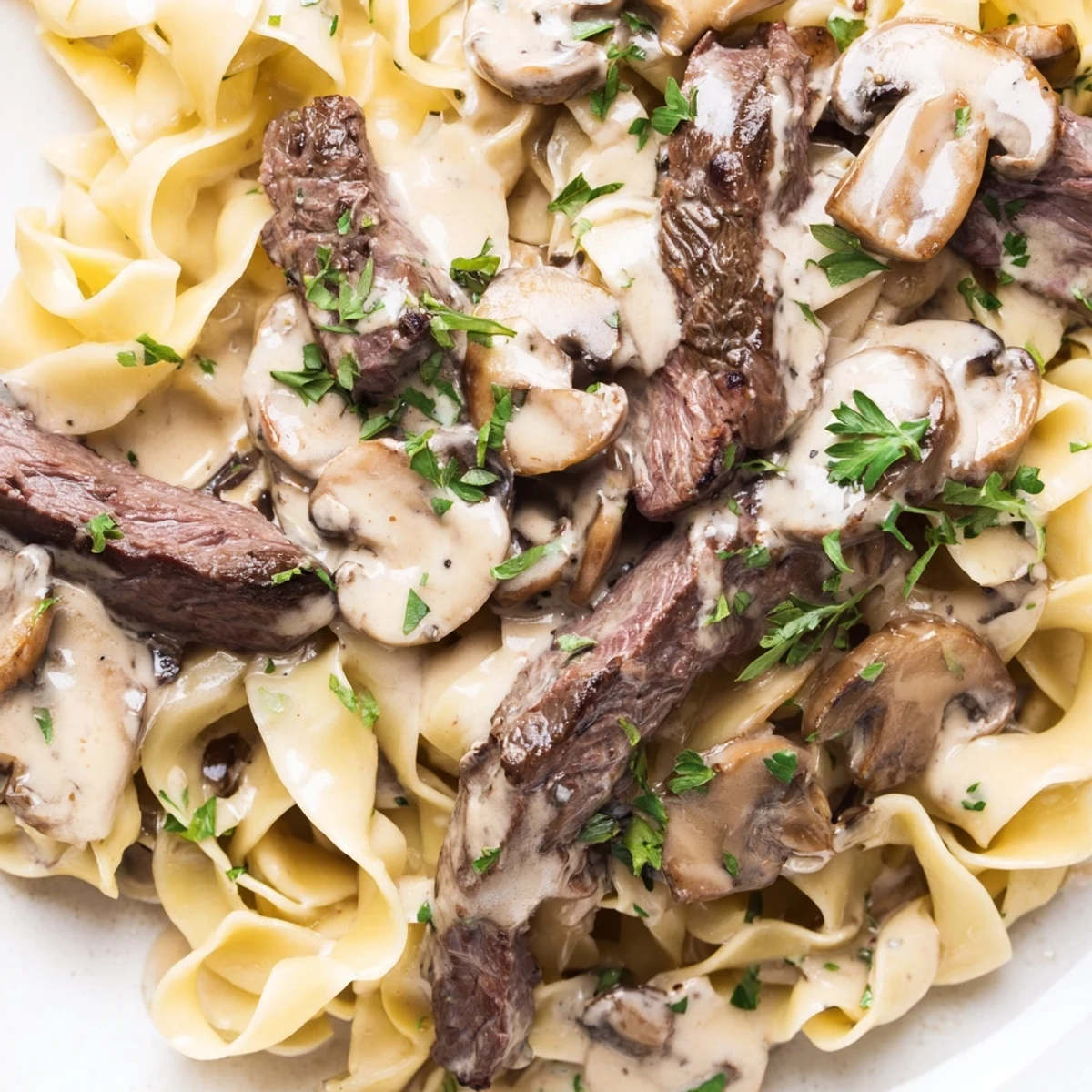 Golden egg noodles topped with rich beef stroganoff, featuring juicy beef strips and mushrooms ready to be enjoyed.