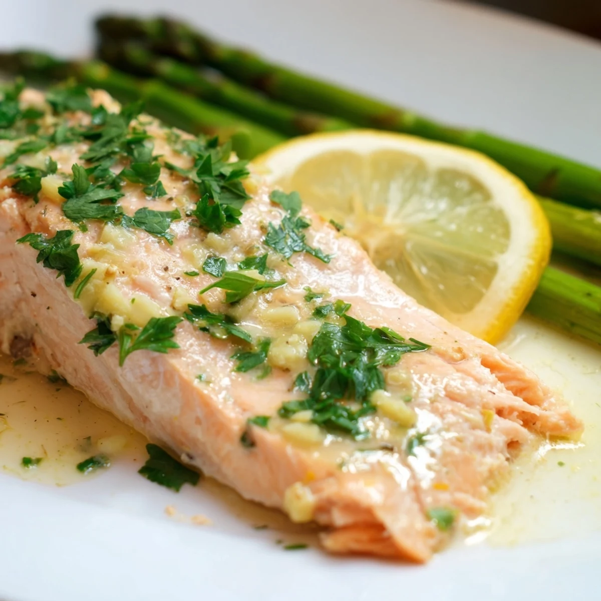 Perfectly flaky and tender Lemon Garlic Butter Salmon with Asparagus Spears served alongside roasted asparagus spears on a white ceramic plate.