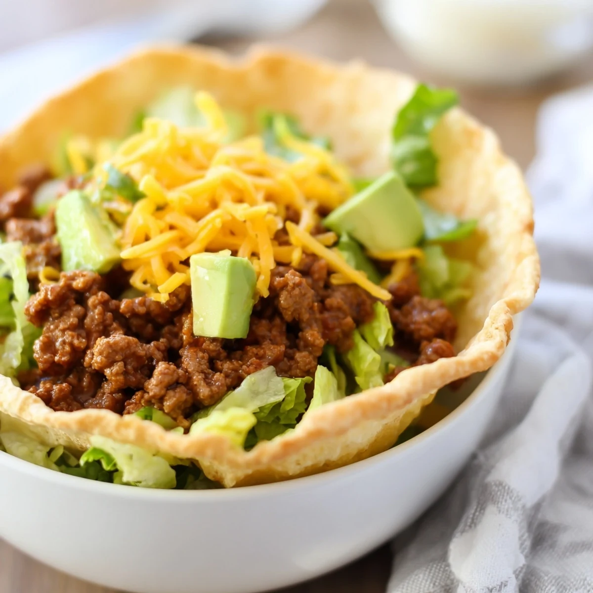 A vibrant beef taco salad in a golden tortilla bowl topped with cherry tomatoes, olives, and avocado.