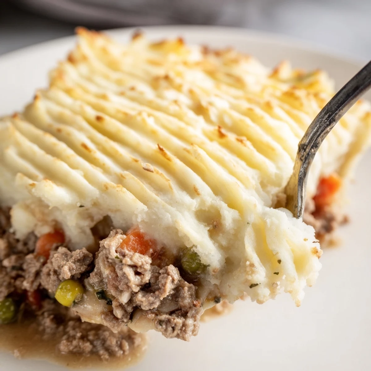 Freshly baked Beef Shepherds Pie with Peas and Carrots sits bubbling from the oven, ready to serve with a rustic wooden spoon.
