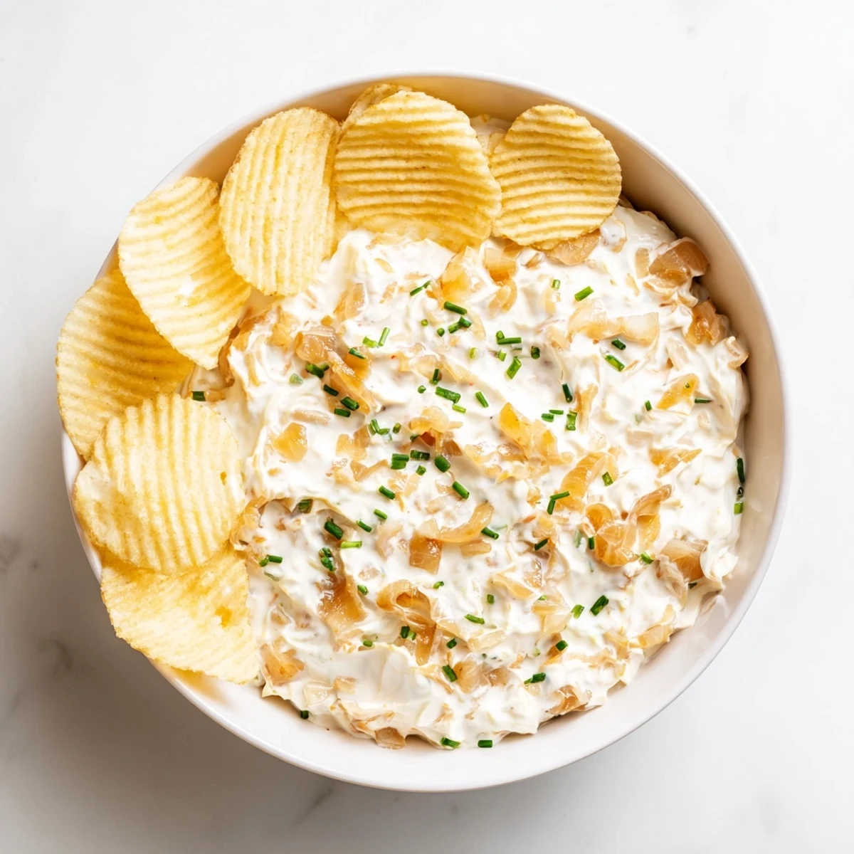 Creamy Game Day Onion Dip served in a bowl, garnished with fresh chives alongside crispy golden potato chips.