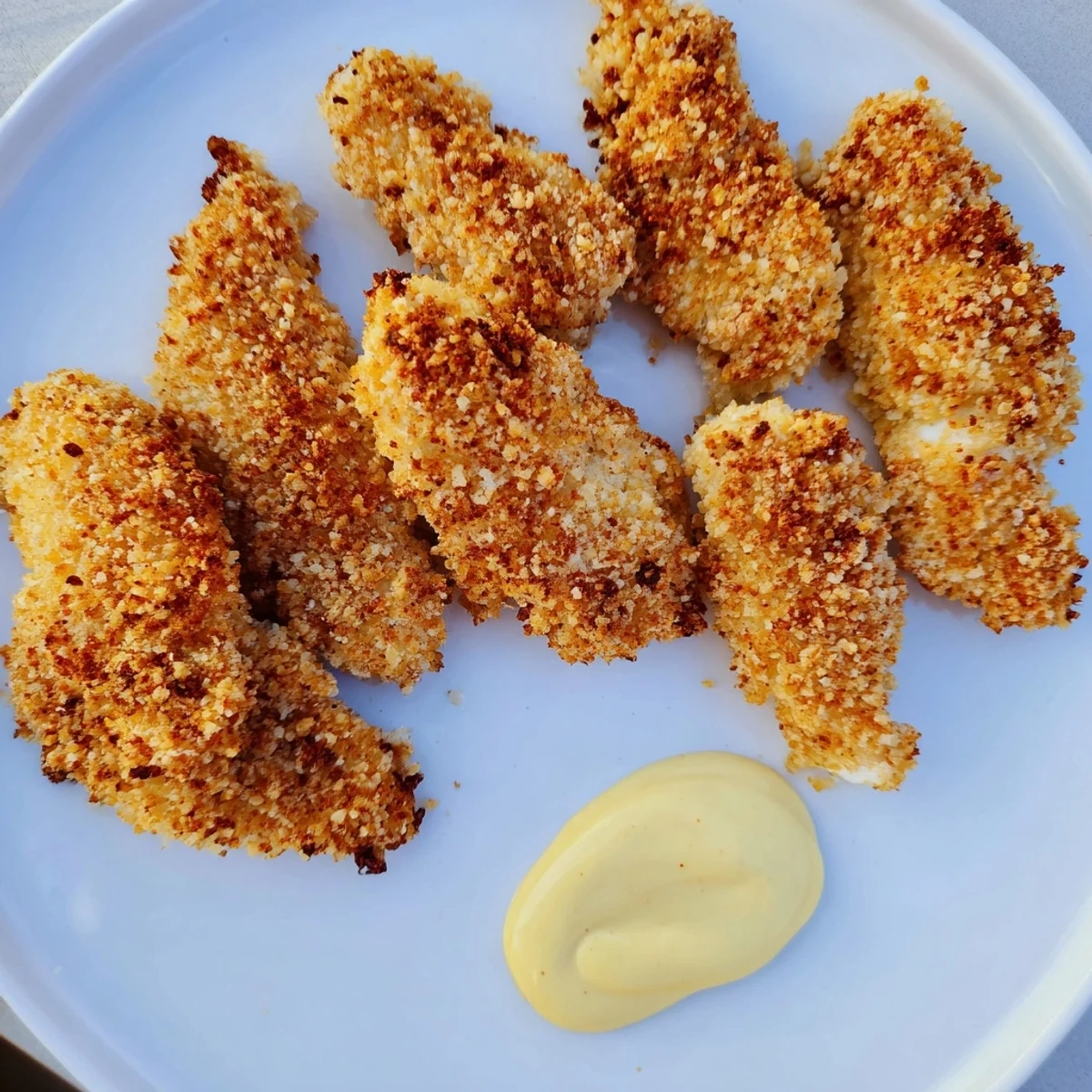 Homemade honey mustard chicken tenders served on a platter with a creamy dipping sauce and a side salad.