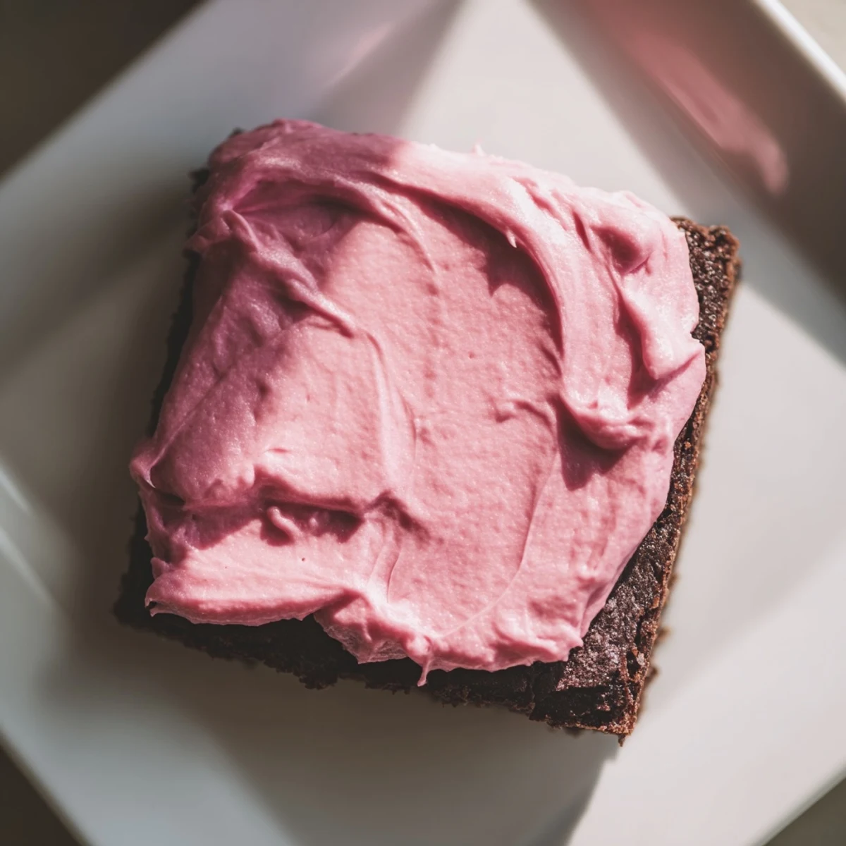 A close-up view of homemade brownies with pink frosting, showcasing the fudgy texture and vibrant pink swirls.