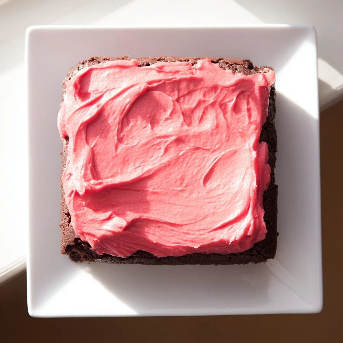 Rich chocolate brownies topped with creamy pink frosting, garnished with a light dusting of powdered sugar.