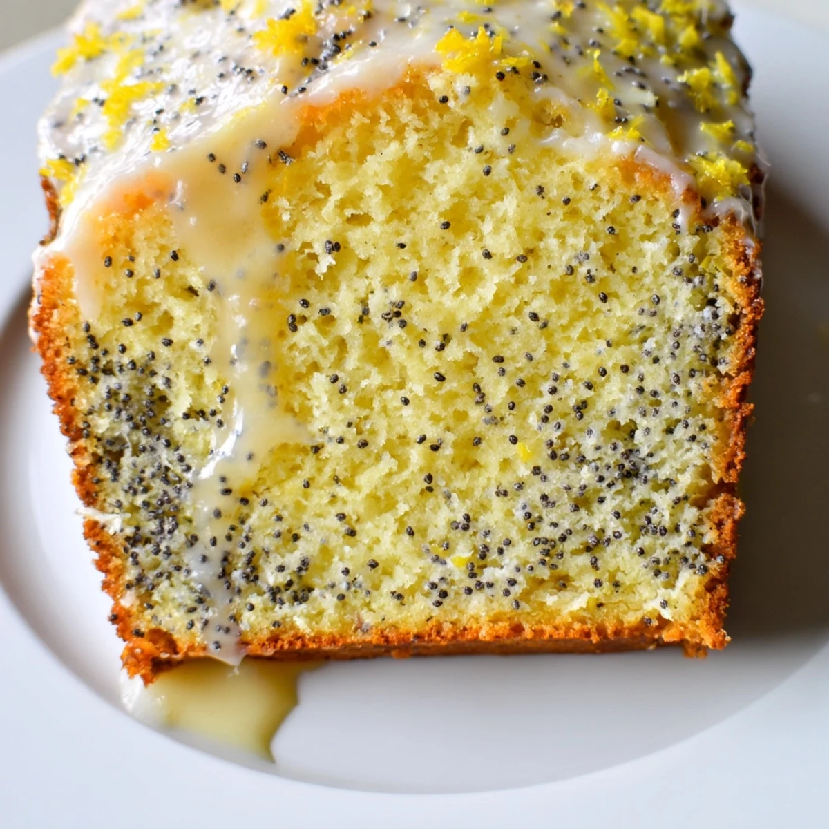 Golden brown Lemon Poppy Seed Loaf on a white plate, the moist interior showing tiny poppy seeds.