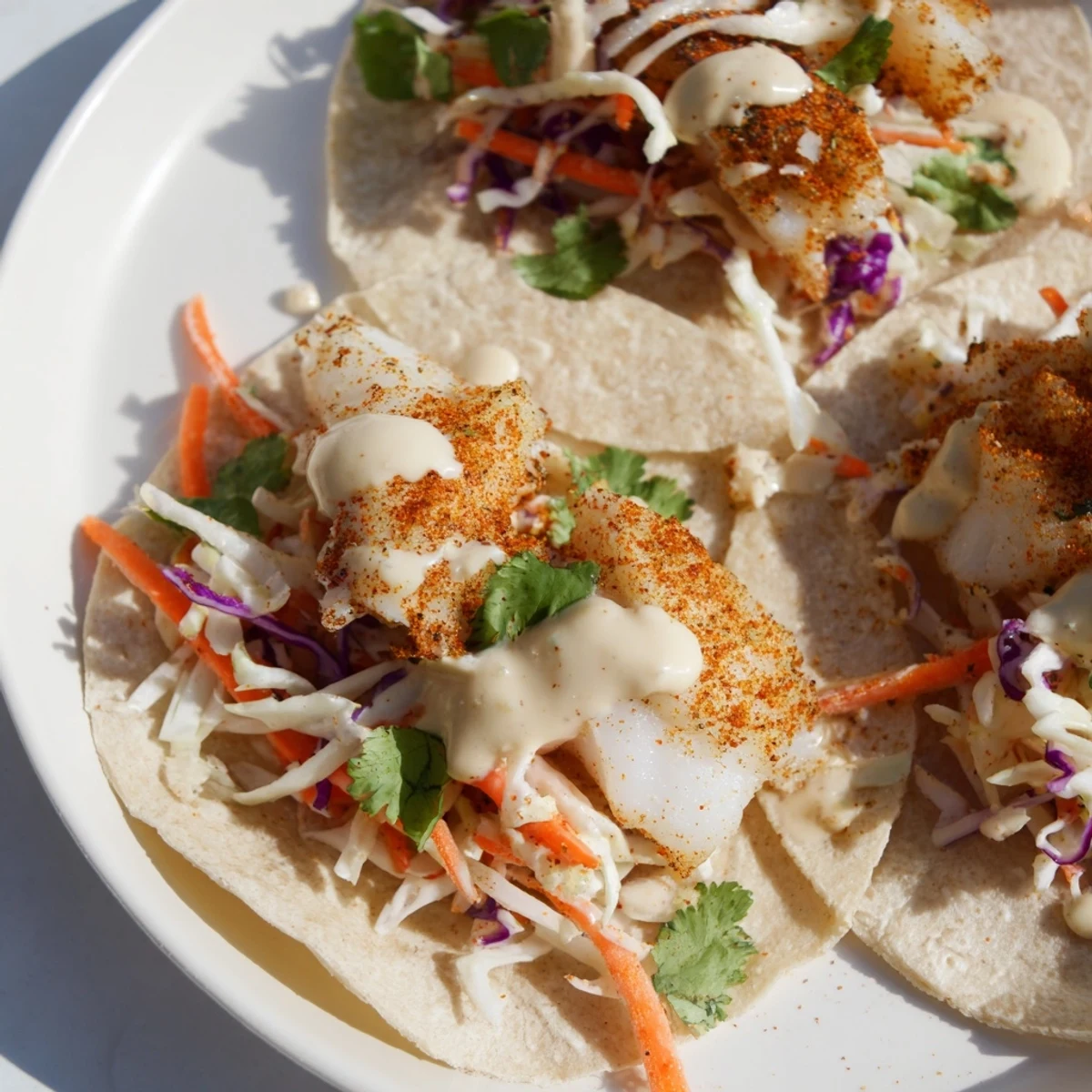 Warm corn tortillas hold Cajun Spiced Fish Tacos with Cabbage Slaw topped with creamy sauce.