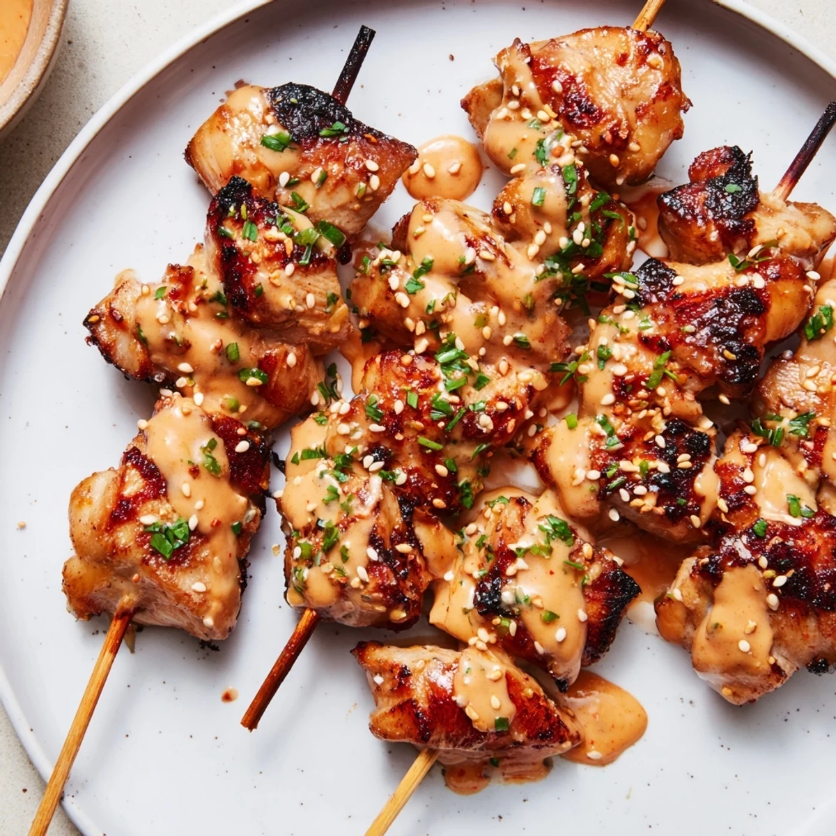 Golden charred Bang Bang Chicken Skewers drizzled with sauce, served over rice for a flavorful party appetizer.