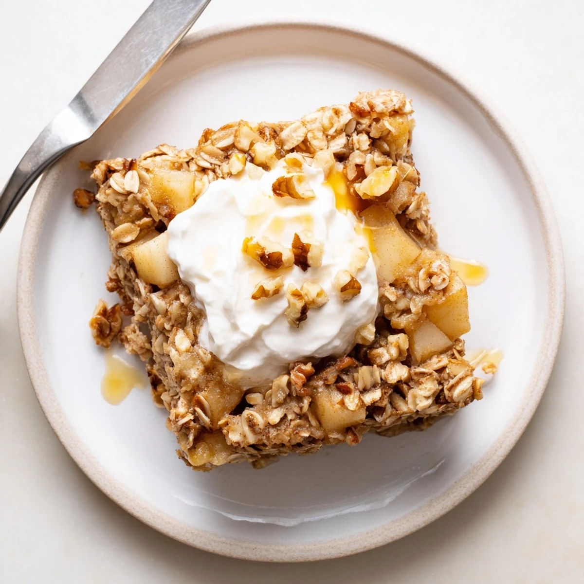 A close-up of golden baked apple oatmeal squares topped with creamy Greek yogurt and chopped walnuts, served on a rustic plate.