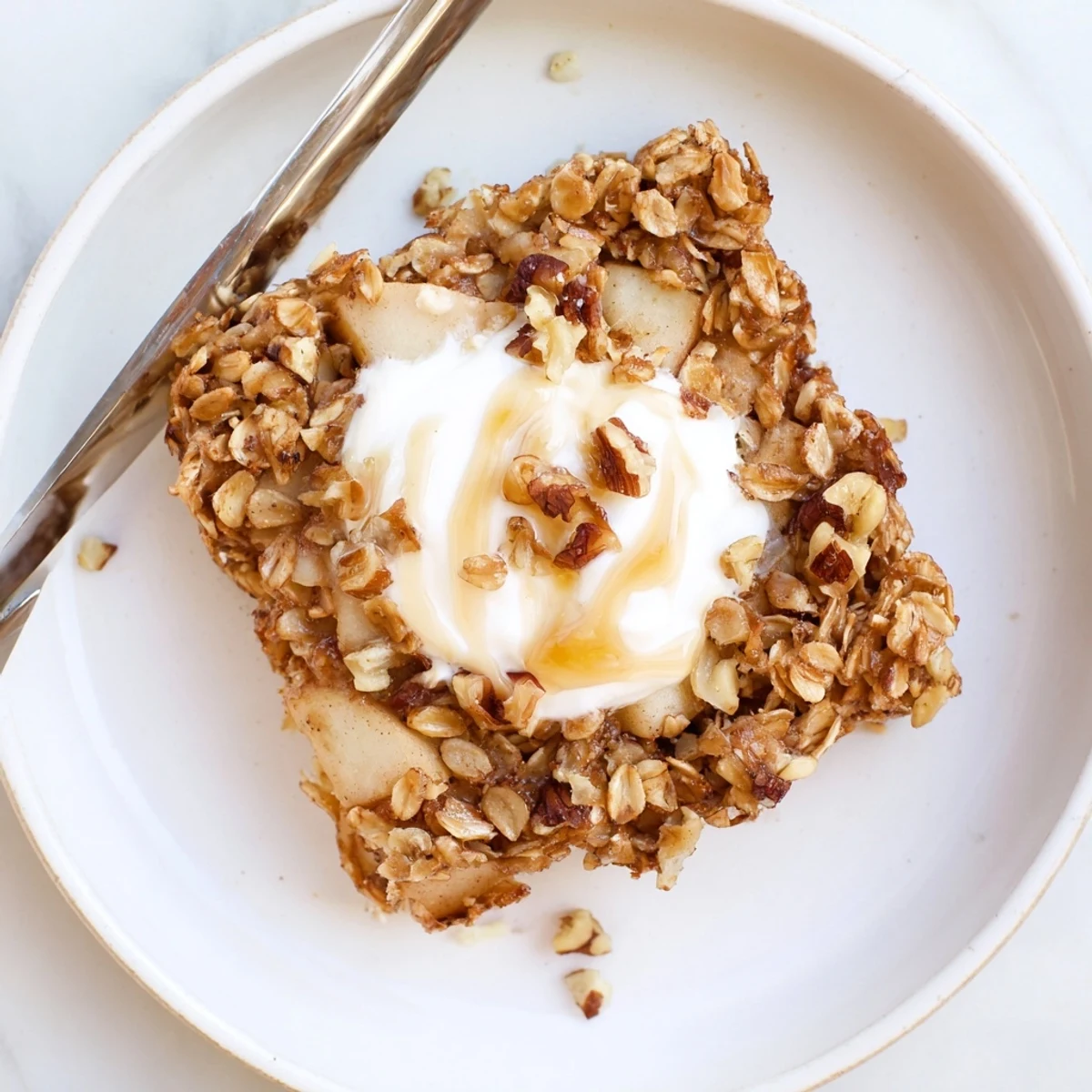 Freshly baked apple oatmeal with Greek yogurt in a white dish, with warm cinnamon apples visible in every bite.