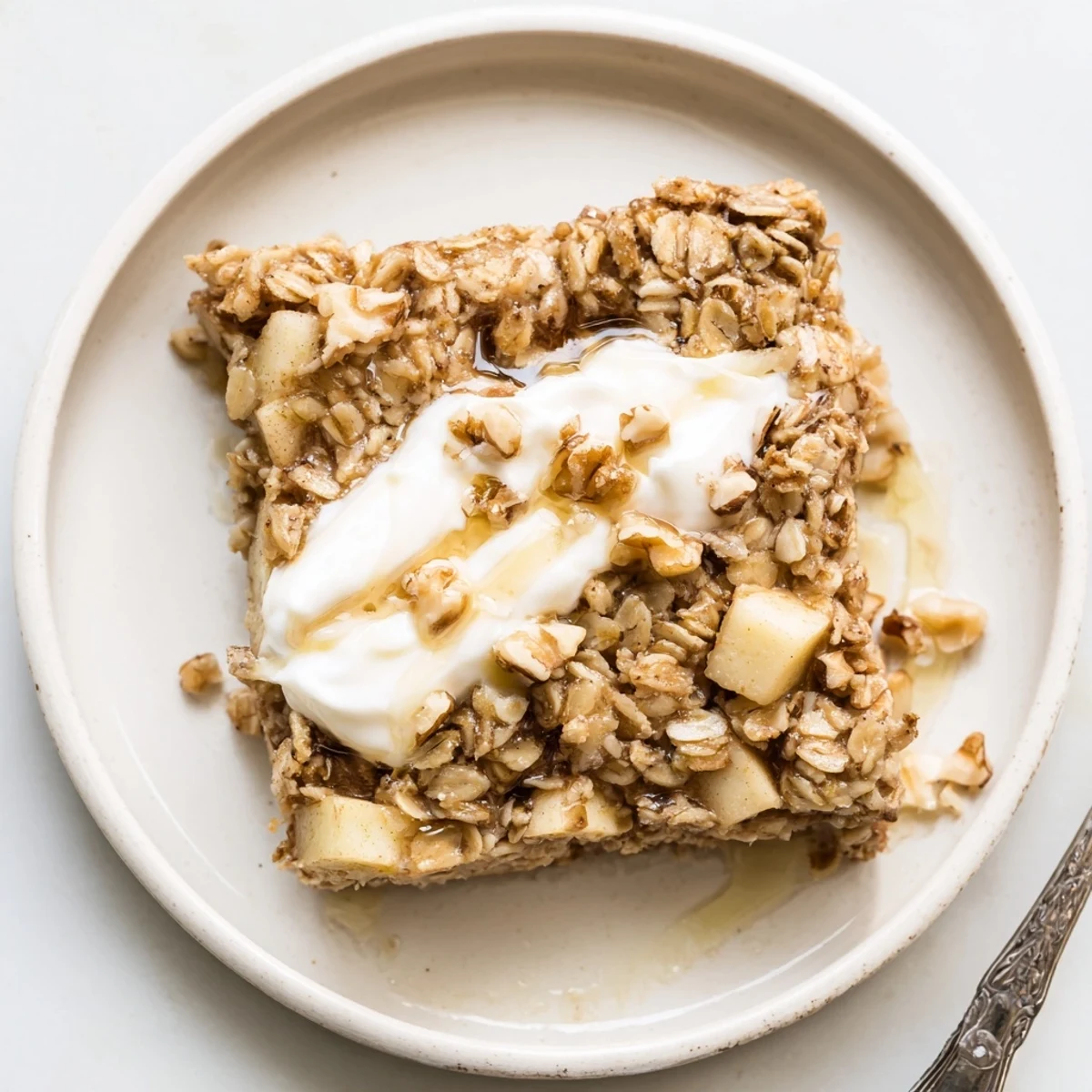 A wholesome slice of baked apple oatmeal with Greek yogurt, drizzled with maple syrup and paired with a hot cup of coffee.