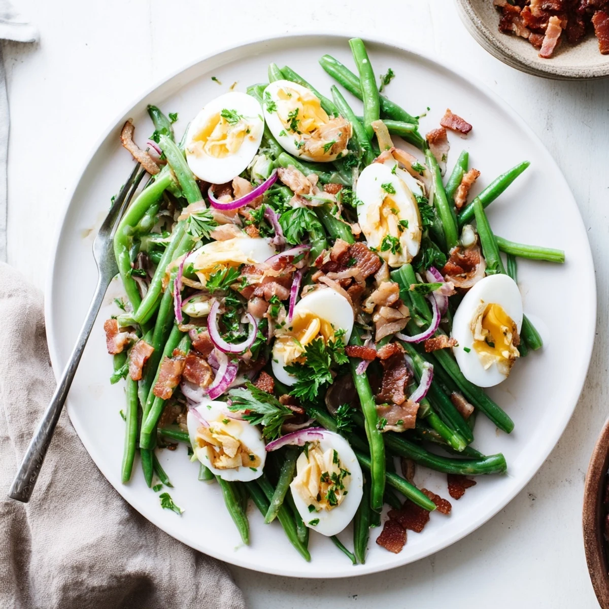 A close-up of Green Bean, Bacon, and Egg Salad shows crisp green beans, crumbled bacon, and creamy quartered eggs on a white plate.