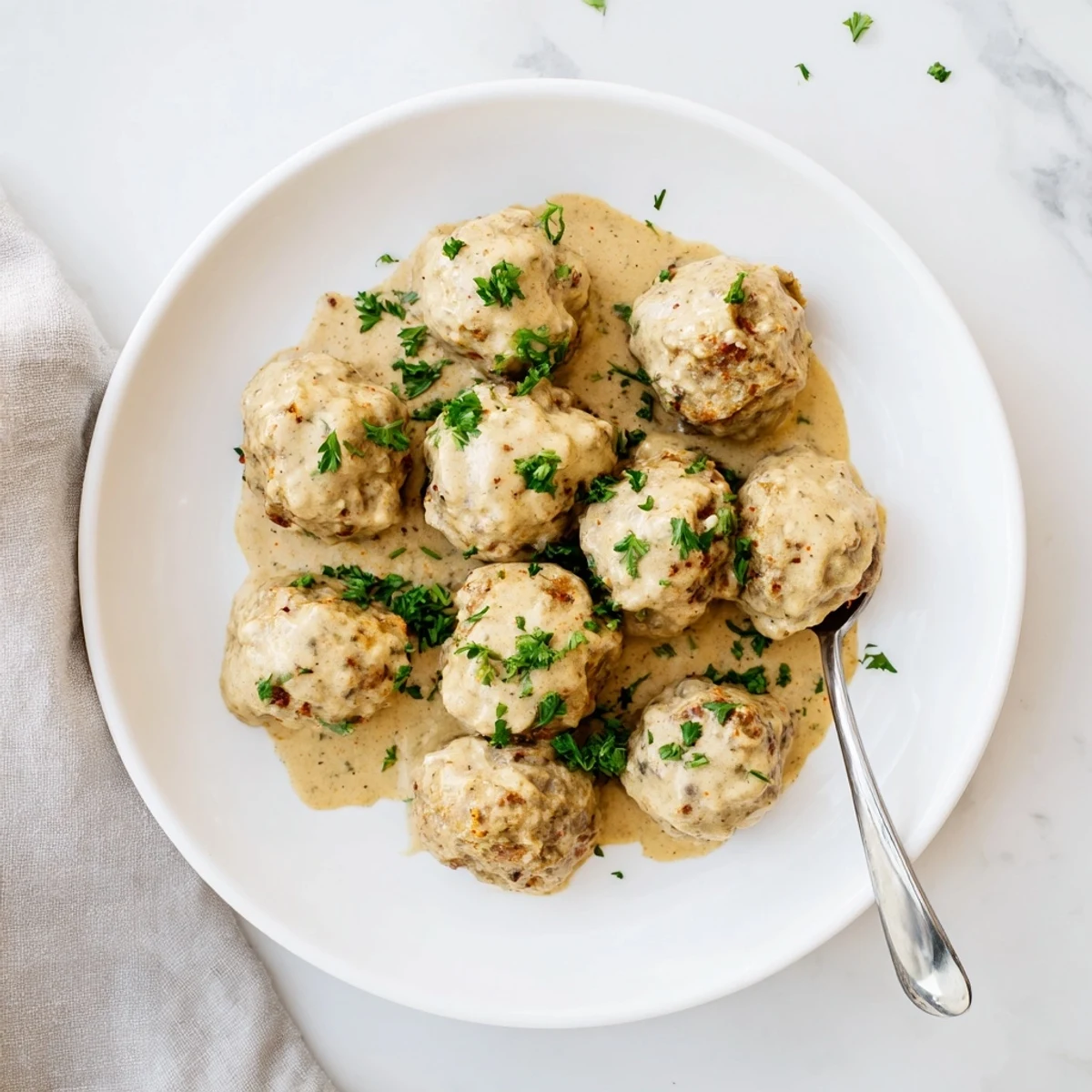 Juicy Chicken and Sun-Dried Tomato Meatballs simmer in a creamy mustard sauce, garnished with fresh parsley on a plate.  