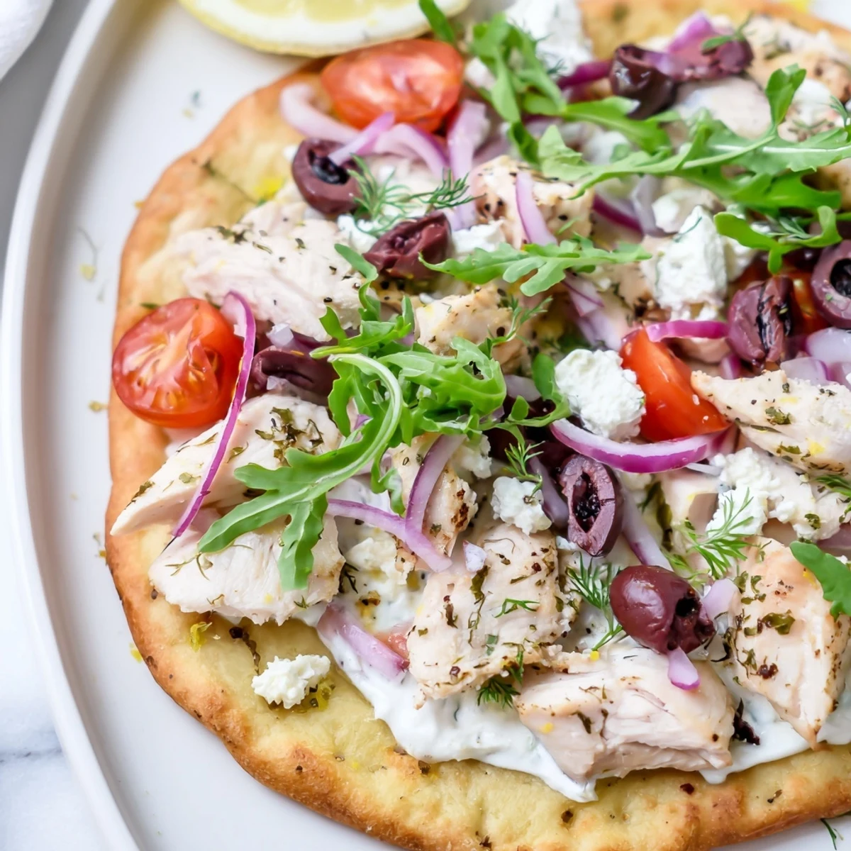 Golden, crispy flatbread topped with lemon-herb chicken, creamy feta, and vibrant cherry tomatoes on a wooden board.
