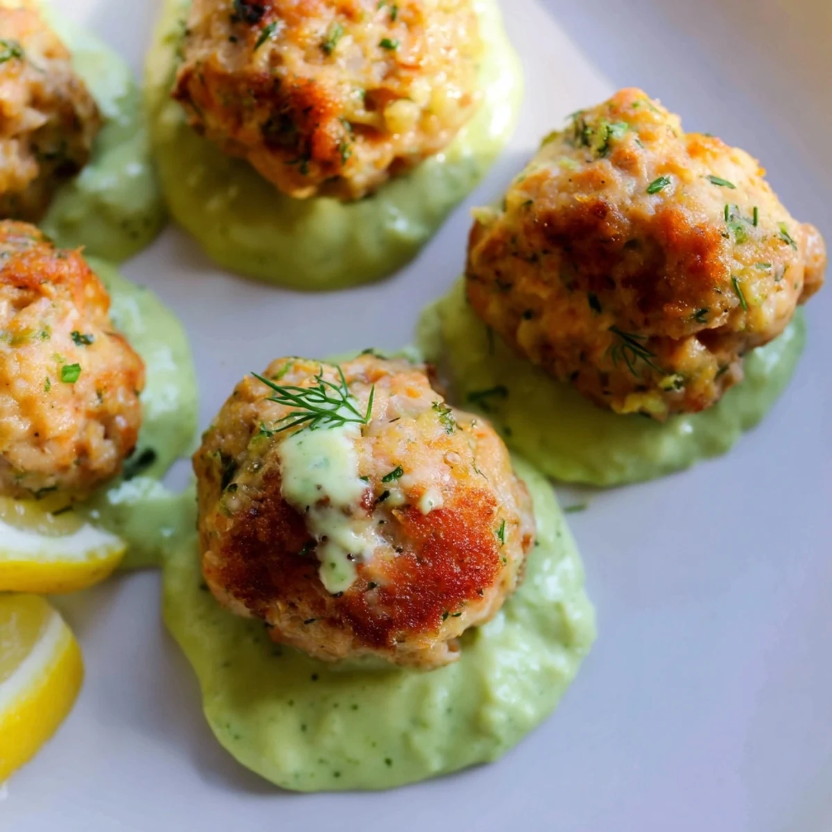 Crispy pan-fried salmon balls arranged on a platter beside a vibrant green avocado yogurt dip, perfect for a gluten-free main dish.