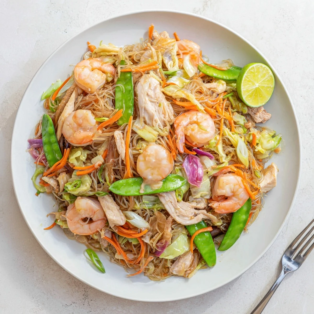 Golden bowl of traditional Pancit Bihon topped with tender chicken, shrimp, and fresh green scallions.
