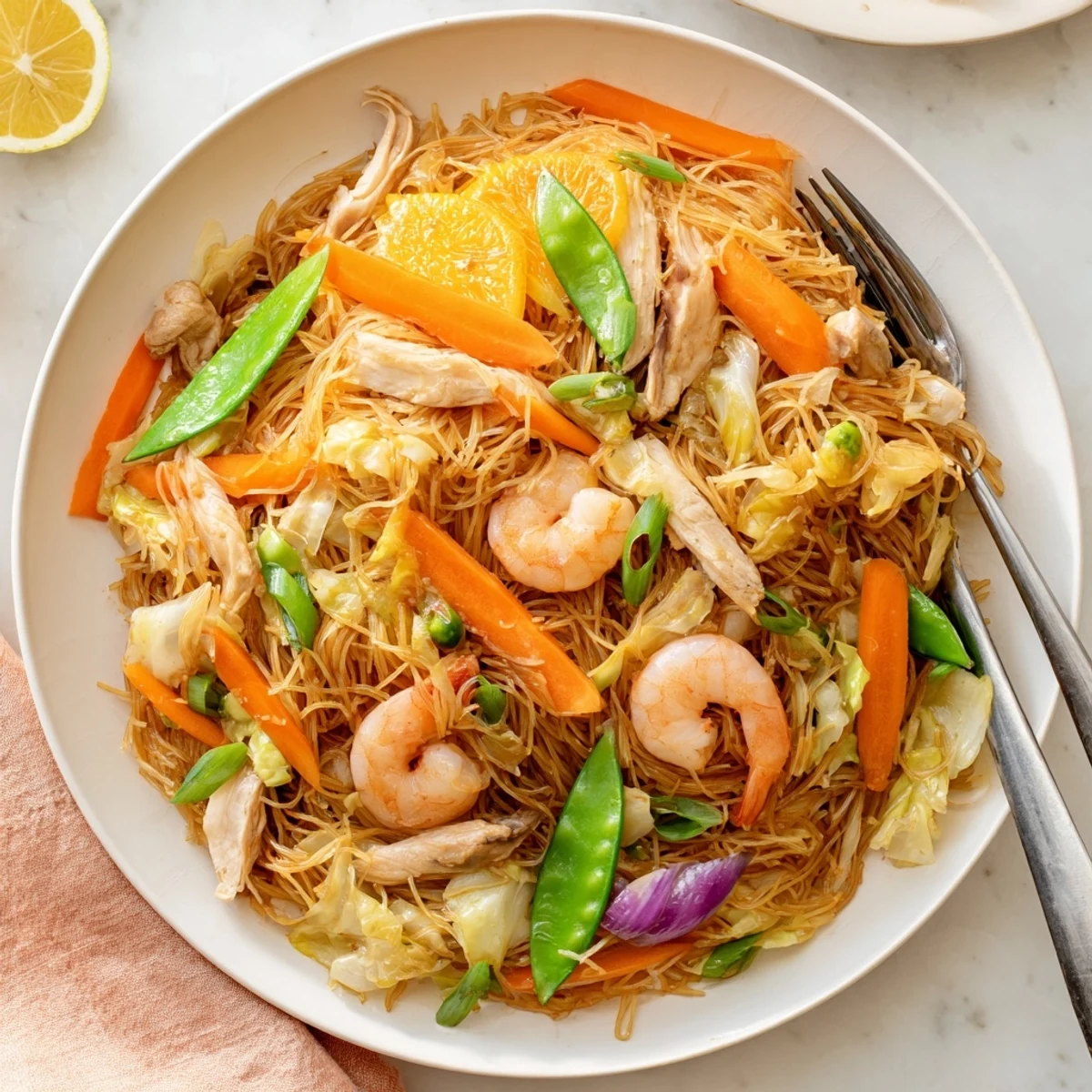 Hearty serving platter of traditional Pancit Bihon garnished with lemon wedges and chopped scallions.