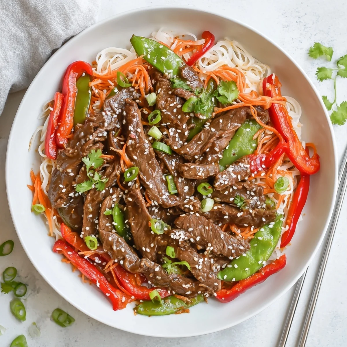 Steaming bowl of sticky beef noodles with sesame garnish and vibrant stir-fried vegetables