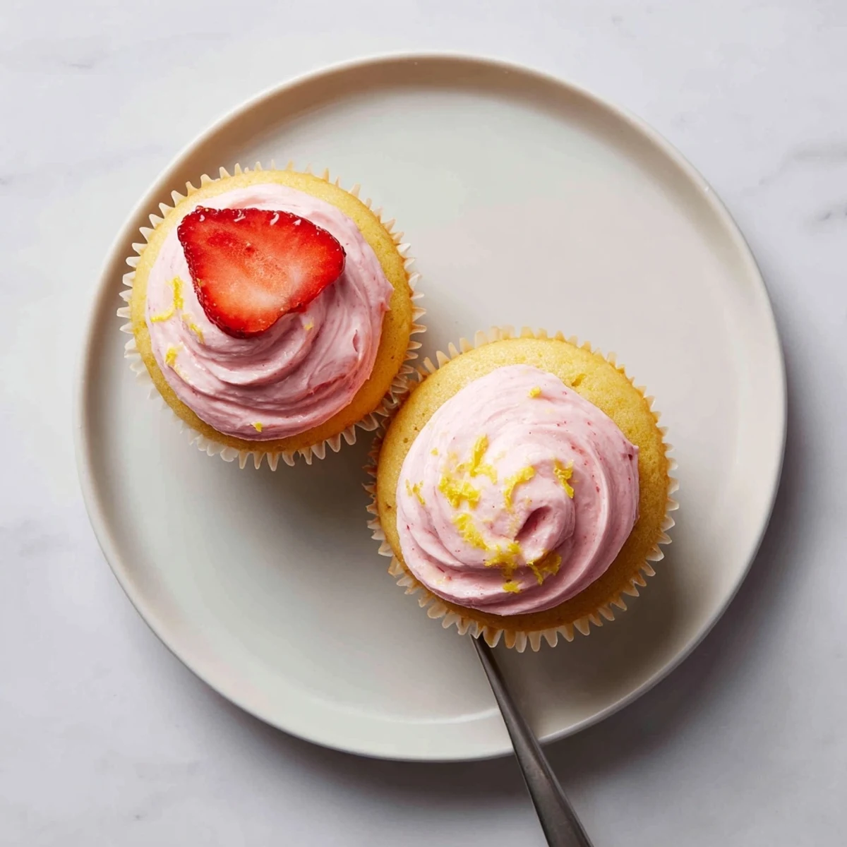Golden lemon cupcakes with fluffy pink strawberry buttercream frosting piped into elegant swirls on a white plate