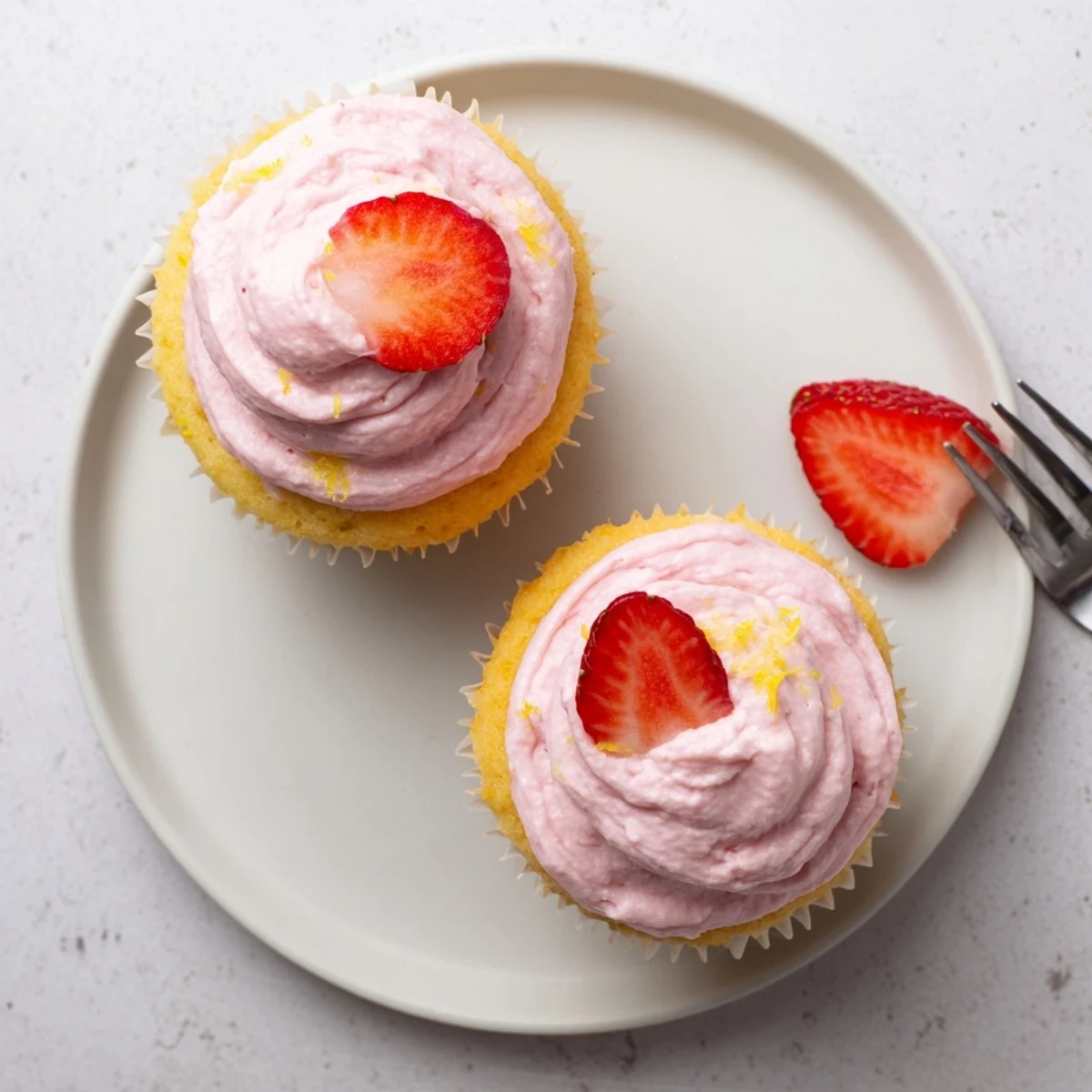 Freshly baked lemon cupcakes topped with naturally sweet strawberry buttercream decorated with lemon zest curls and strawberry slices