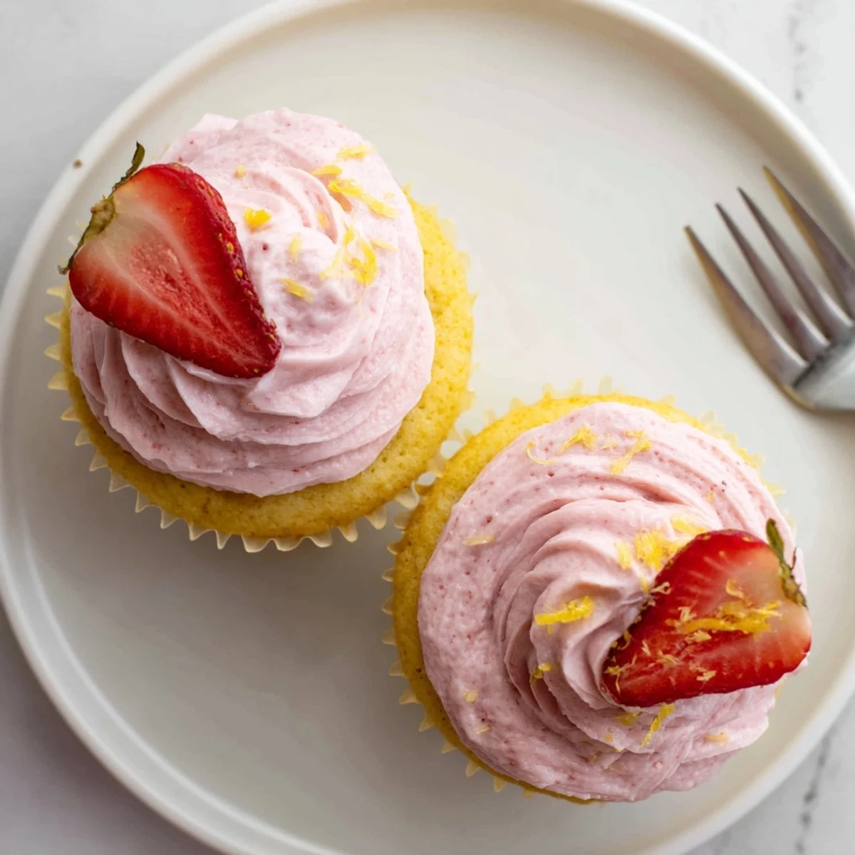 Soft zesty lemon cupcakes crowned with vibrant pink strawberry frosting garnished with fresh fruit for spring dessert presentations