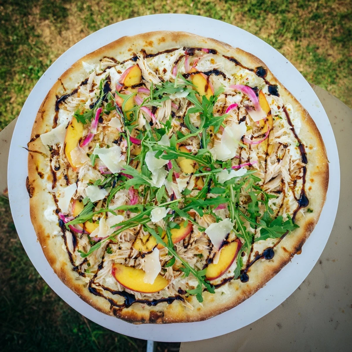 Sliced Chicken Peach Ricotta Pizza on wooden board featuring wilted arugula and dark balsamic swirls