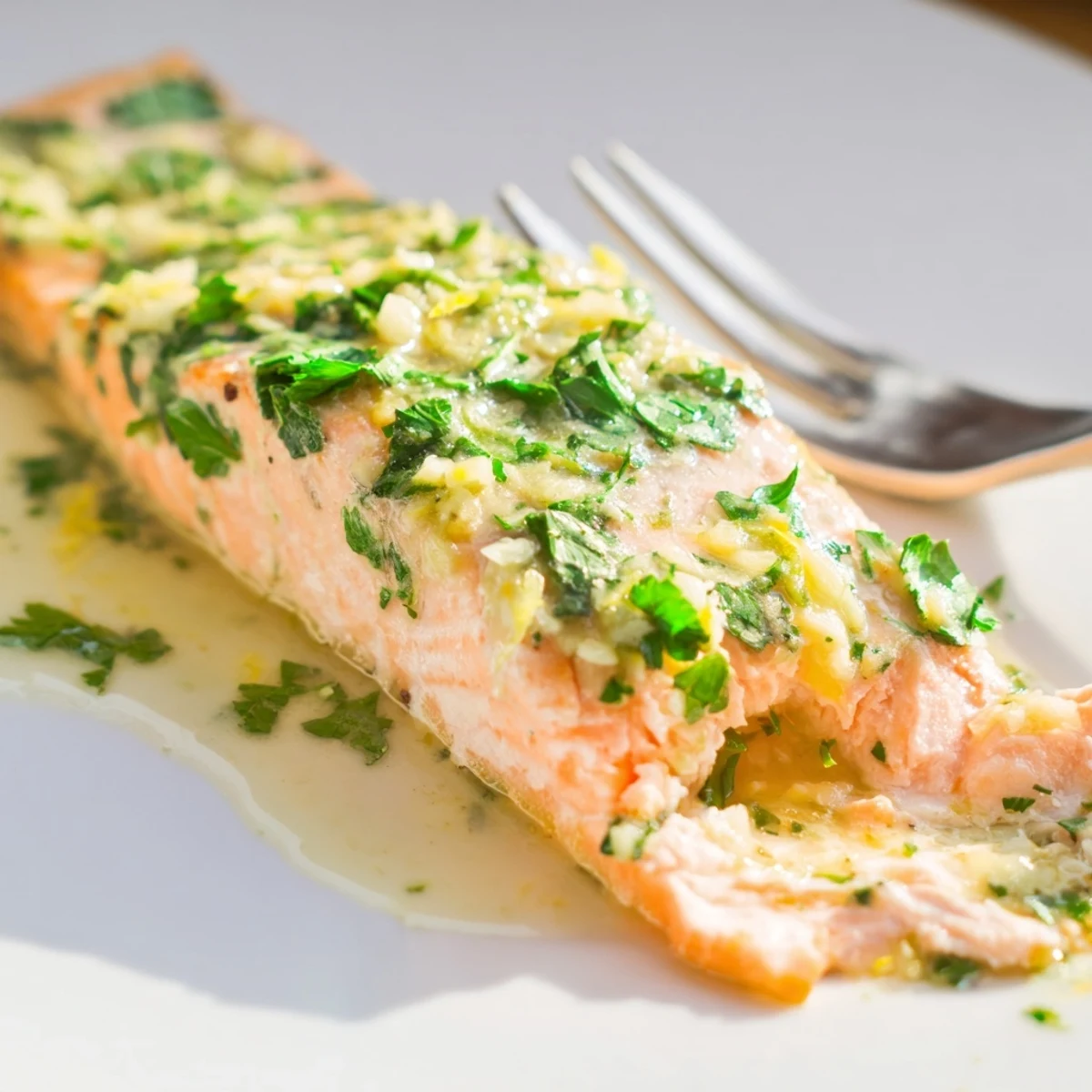 Flaky tender salmon baked in rich melted garlic butter sauce with zesty lemon garnish and chopped herbs