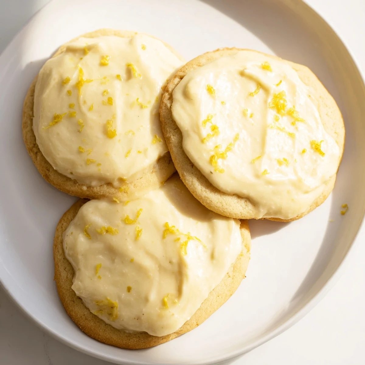 Soft lemon frosted cookies topped with tangy white glaze on a white plate