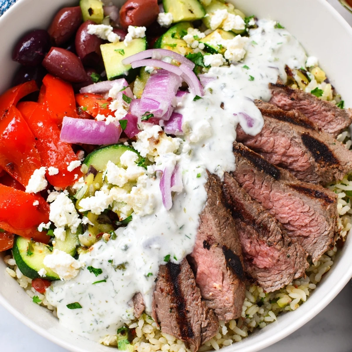 Colorful Mediterranean steak bowl arranged with fresh cucumber, red onion, roasted peppers, and zesty yogurt dressing