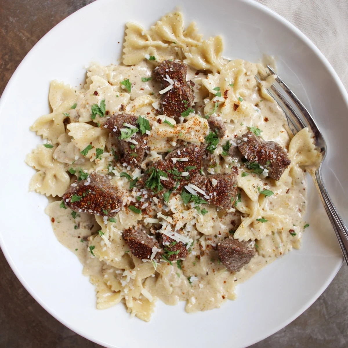 Plated Cajun cream cheese Alfredo bowties garnished with savory spiced beef strips