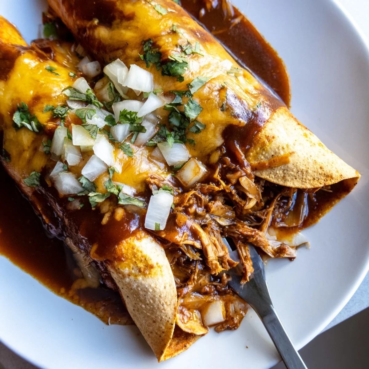 Golden birria enchiladas smothered in melted cheese and rich consommé with fresh cilantro garnish