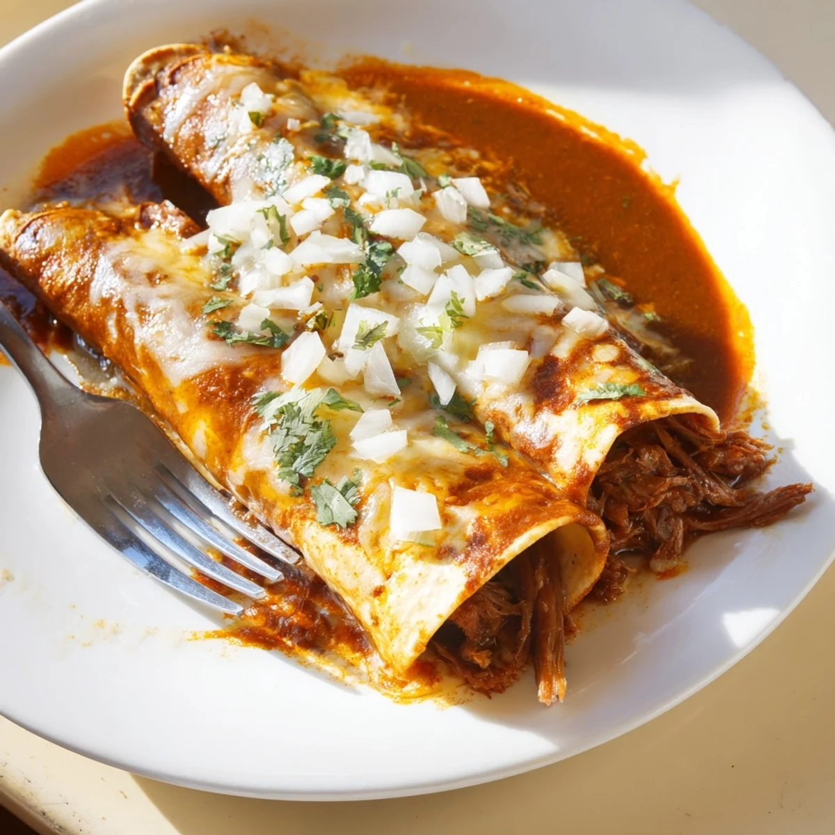 Steaming plate of birria enchiladas drizzled with savory consommé and topped with lime wedges and cilantro