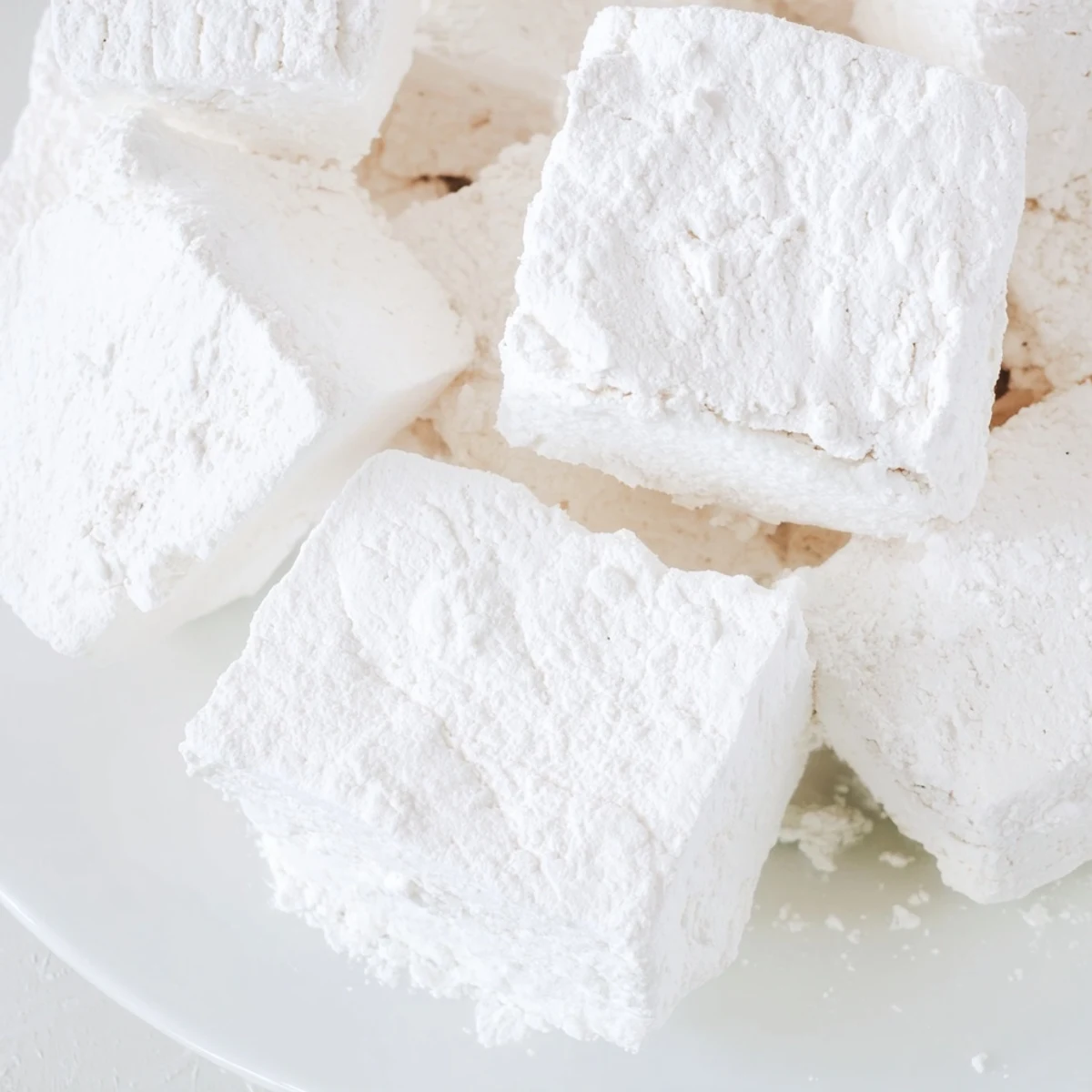 Soft fluffy homemade marshmallows dusted with powdered sugar arranged on a white plate