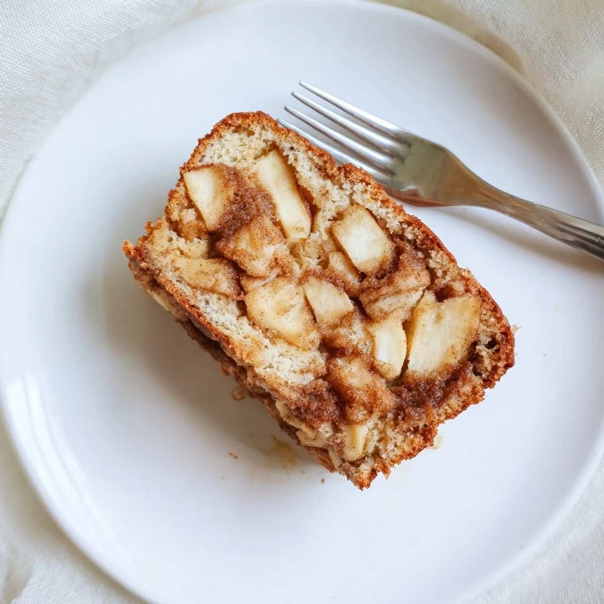 Thick slice of moist cinnamon apple bread on a white plate, perfect for breakfast or dessert