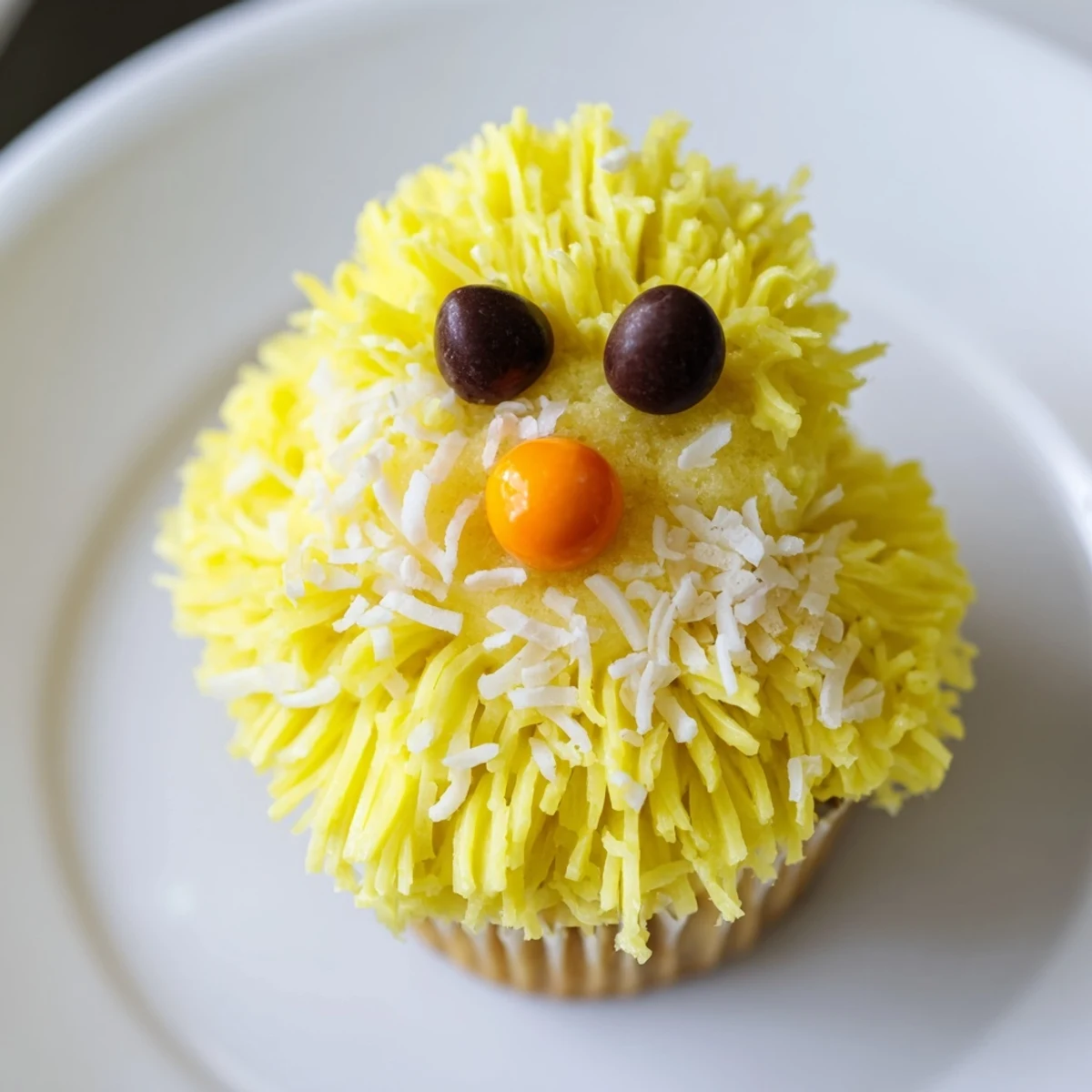 Bright yellow Easter Chick Cupcakes topped with coconut feathers, chocolate chip eyes, and orange candy beaks.