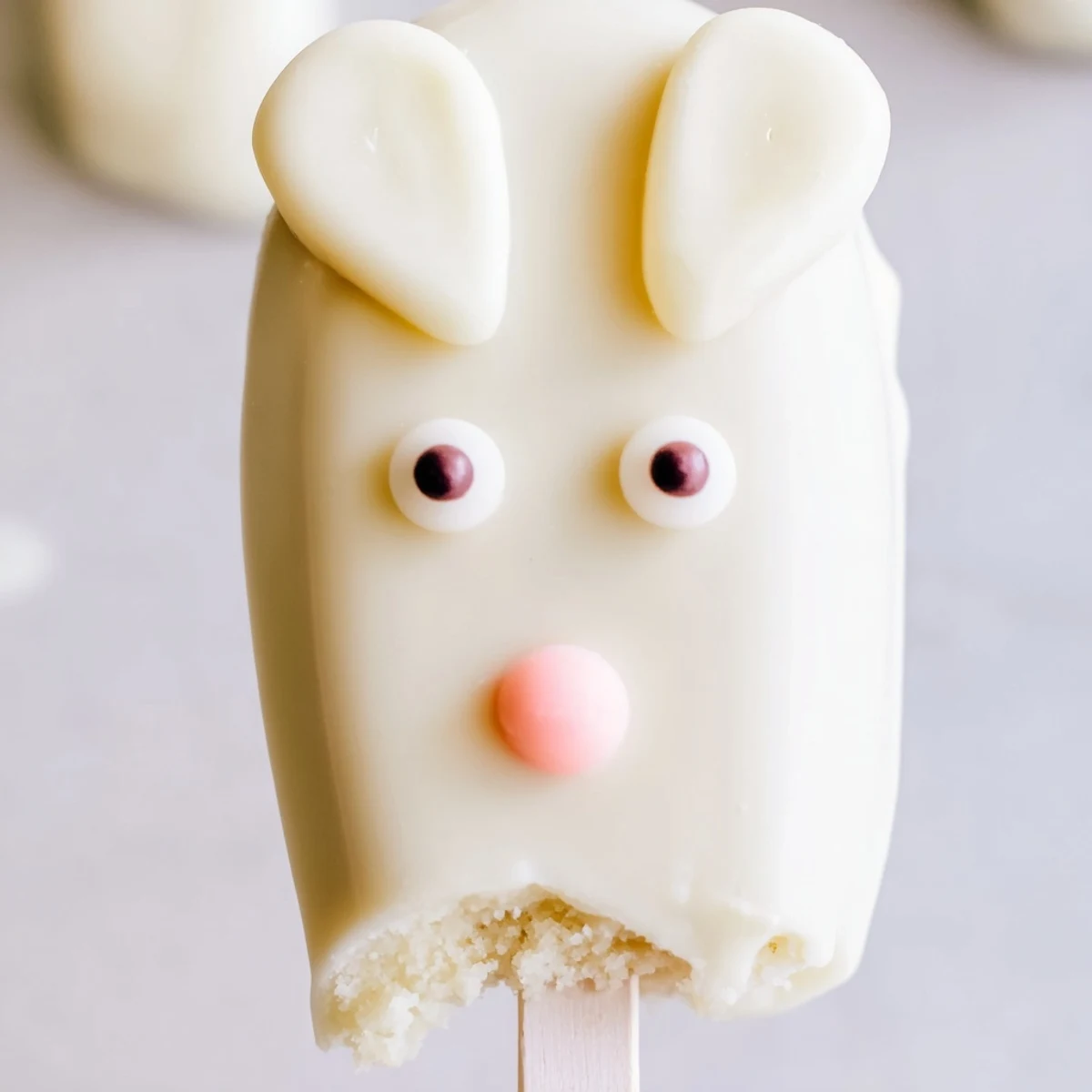 Adorable white chocolate bunny cakesicles with candy eyes on a parchment-lined baking sheet