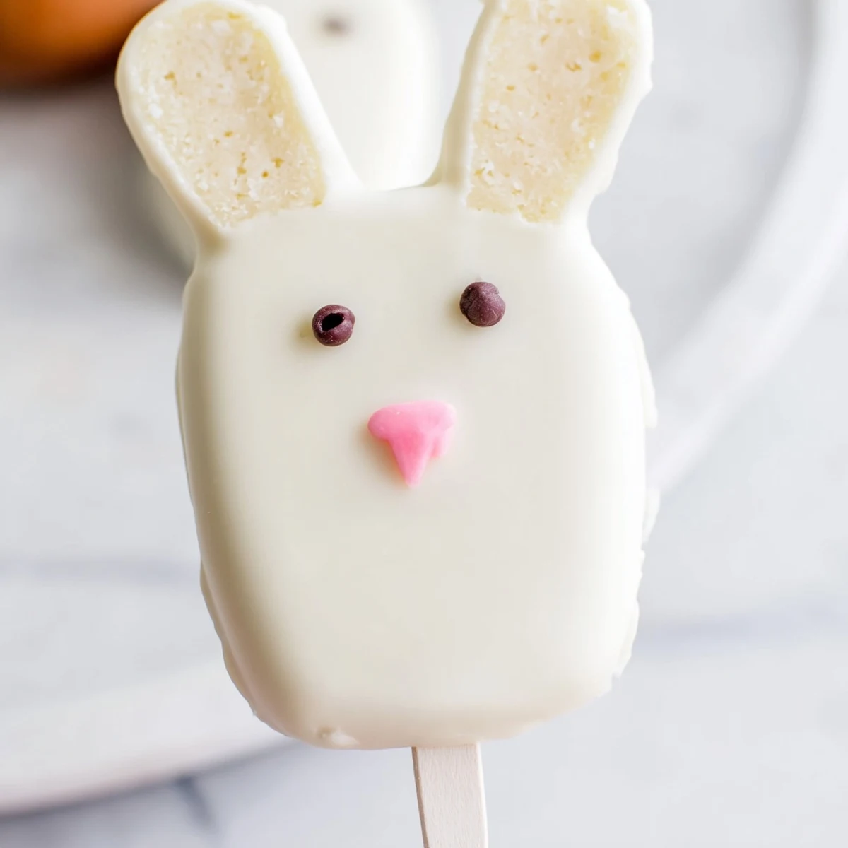 Festive bunny cakesicles coated in creamy white chocolate with pink fondant ears
