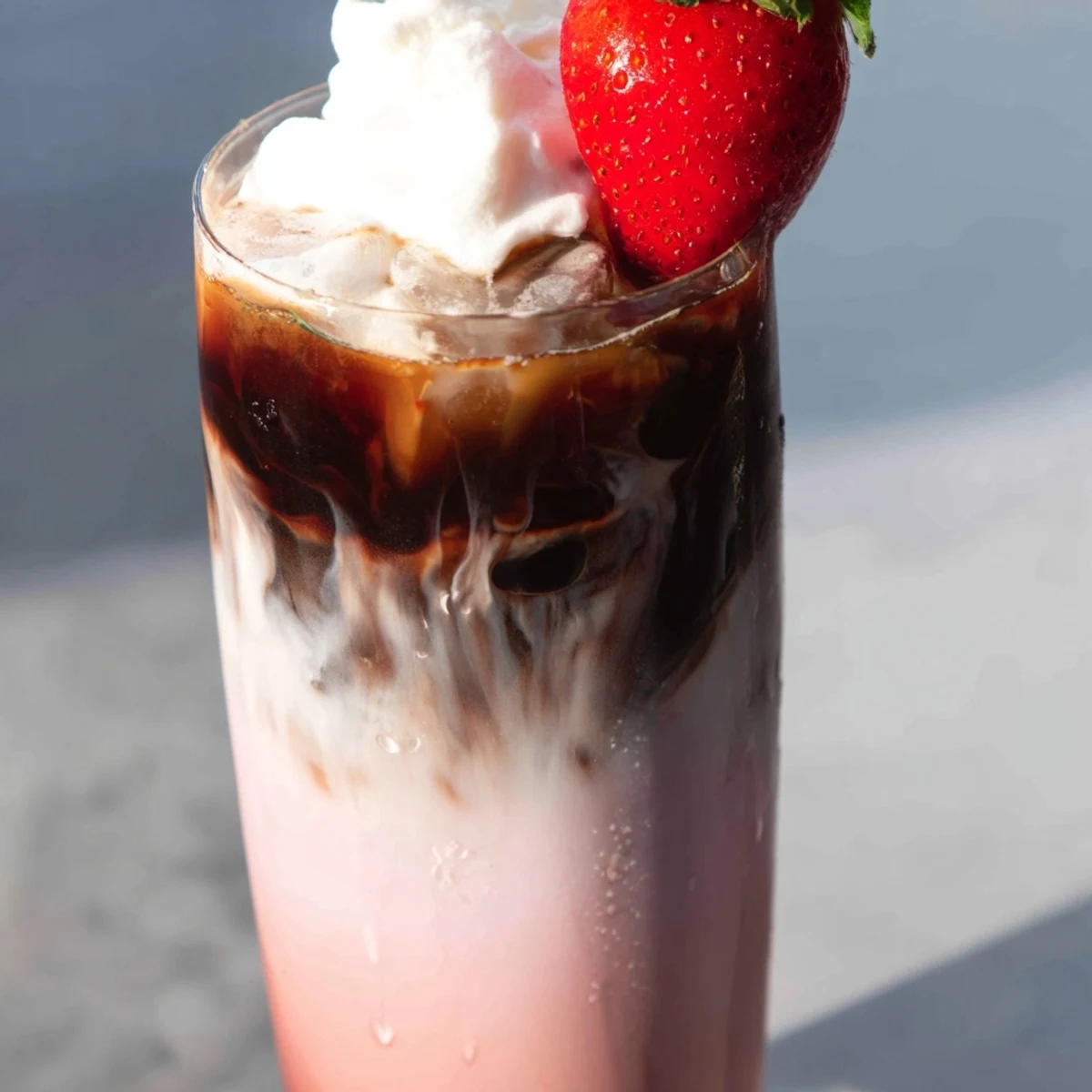 Creamy strawberry cold latte in a tall glass topped with fluffy whipped cream and fresh berry garnish