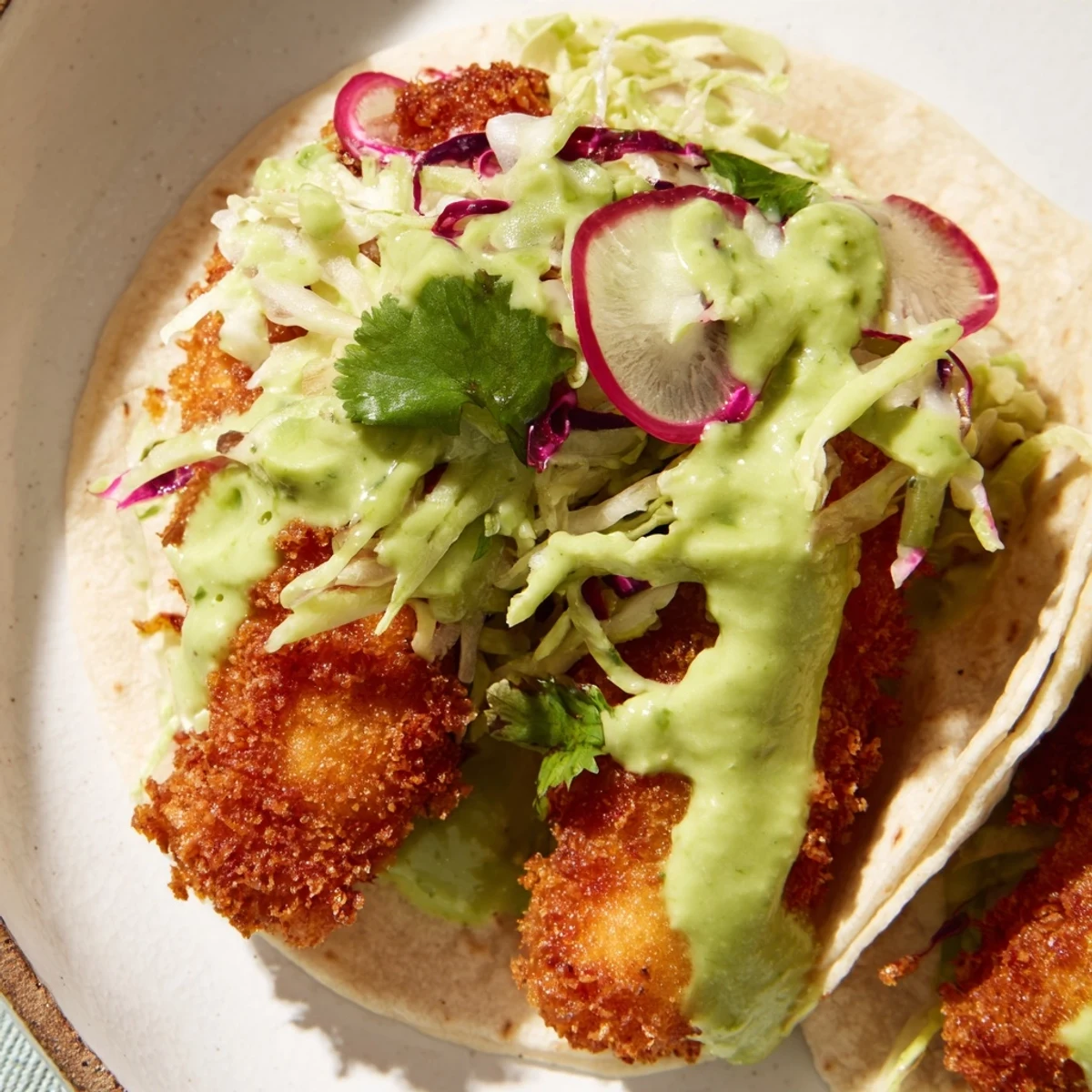 Crispy battered Baja fish tacos nestled in tortillas with tangy slaw and creamy green avocado sauce