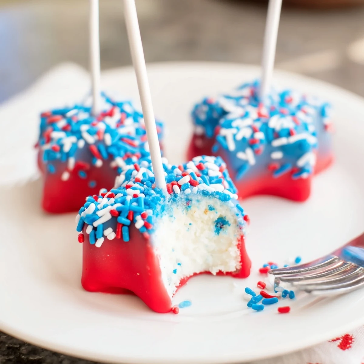 Brightly decorated Fourth Of July Star Cheesecake Pops on parchment, creamy centers visible.