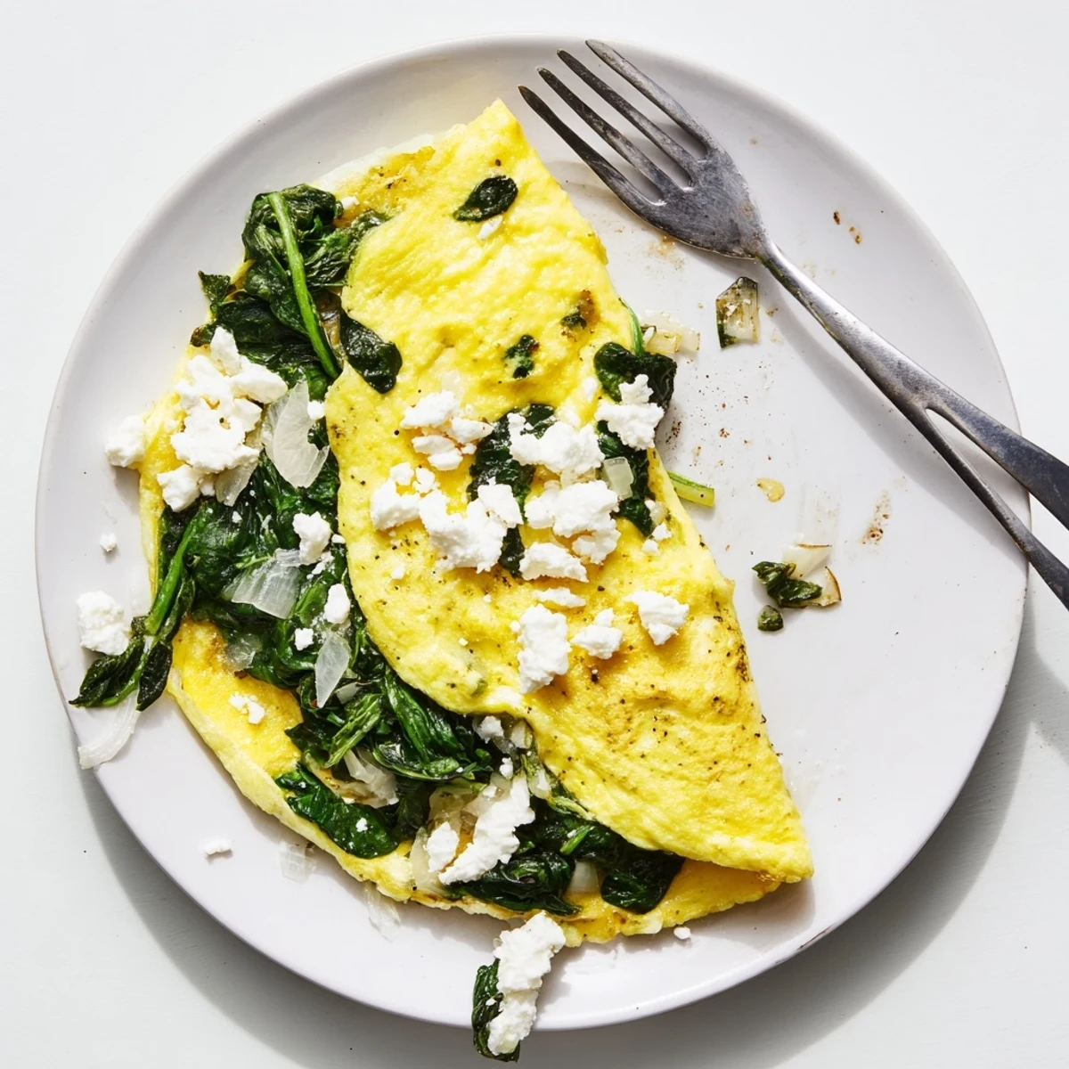 Golden spinach feta omelet folded over wilted greens and creamy crumbled cheese