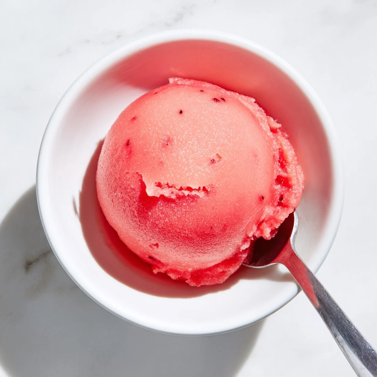 Fresh pink watermelon sorbet scooped into a chilled bowl with lime zest garnish