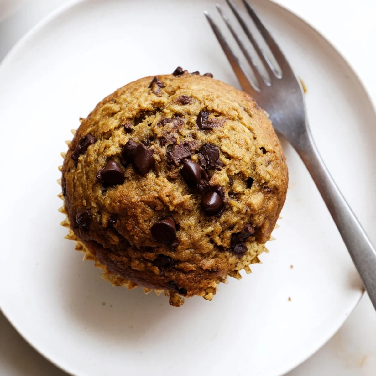 Golden banana espresso chocolate chip muffins topped with melty chocolate chunks on a wooden board