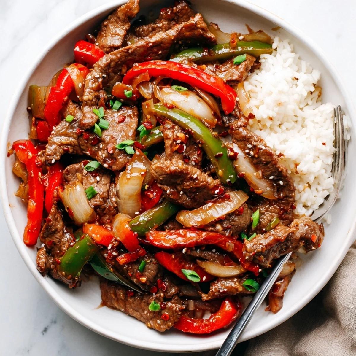 Spicy beef stir fry with chili garlic plated over fluffy white jasmine rice and garnished with fresh green spring onions