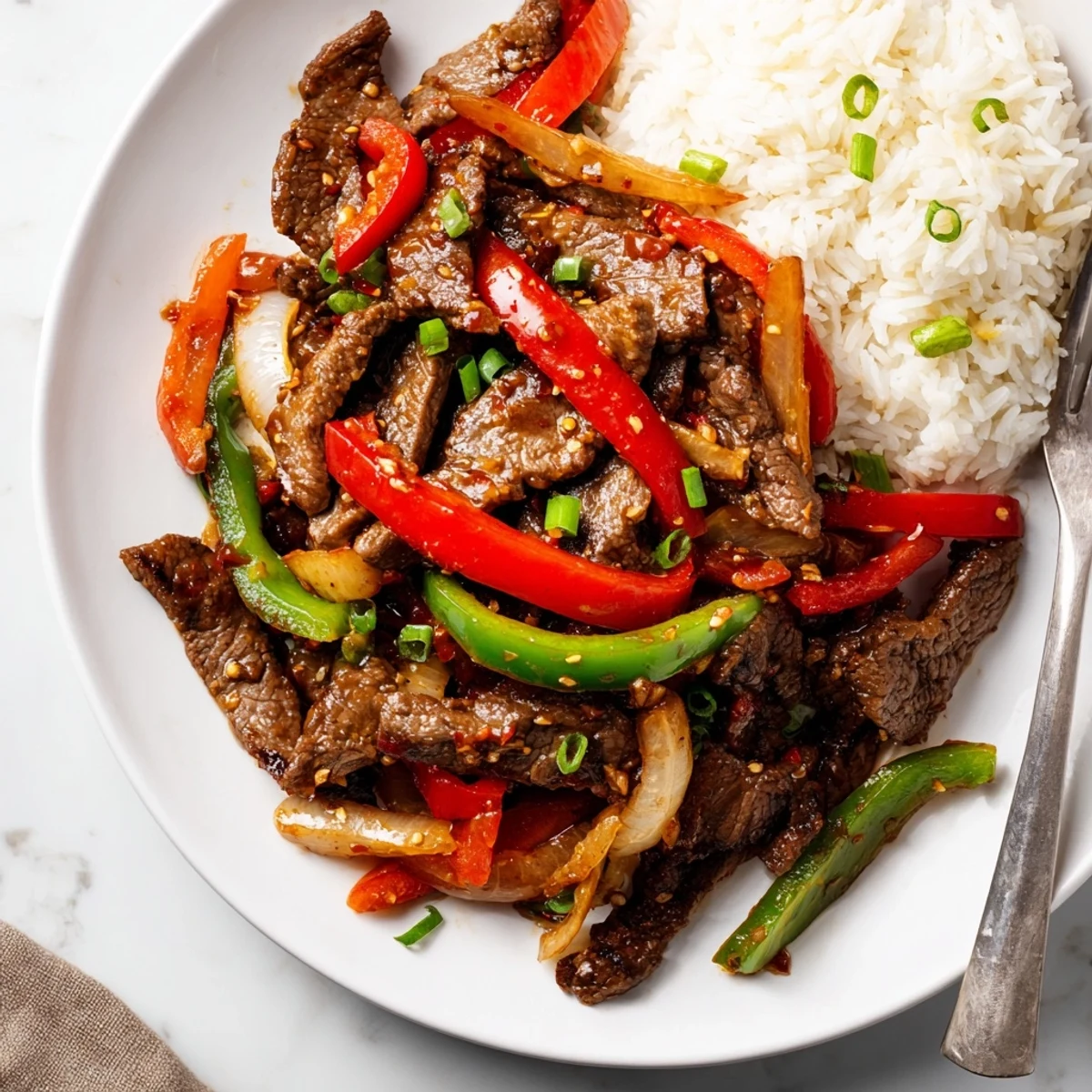 Close up of spicy beef stir fry with chili garlic showcasing thinly sliced sirloin beef and vibrant red and green pepper strips in aromatic sauce