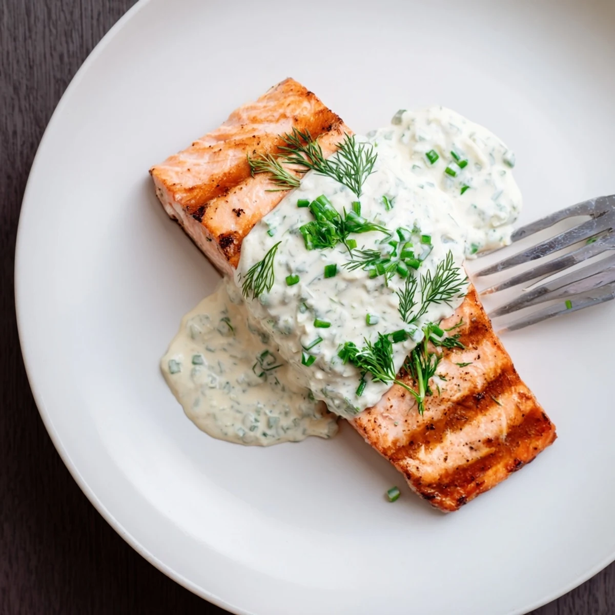Golden grilled salmon fillets with charred grill marks topped with creamy cucumber dill sauce