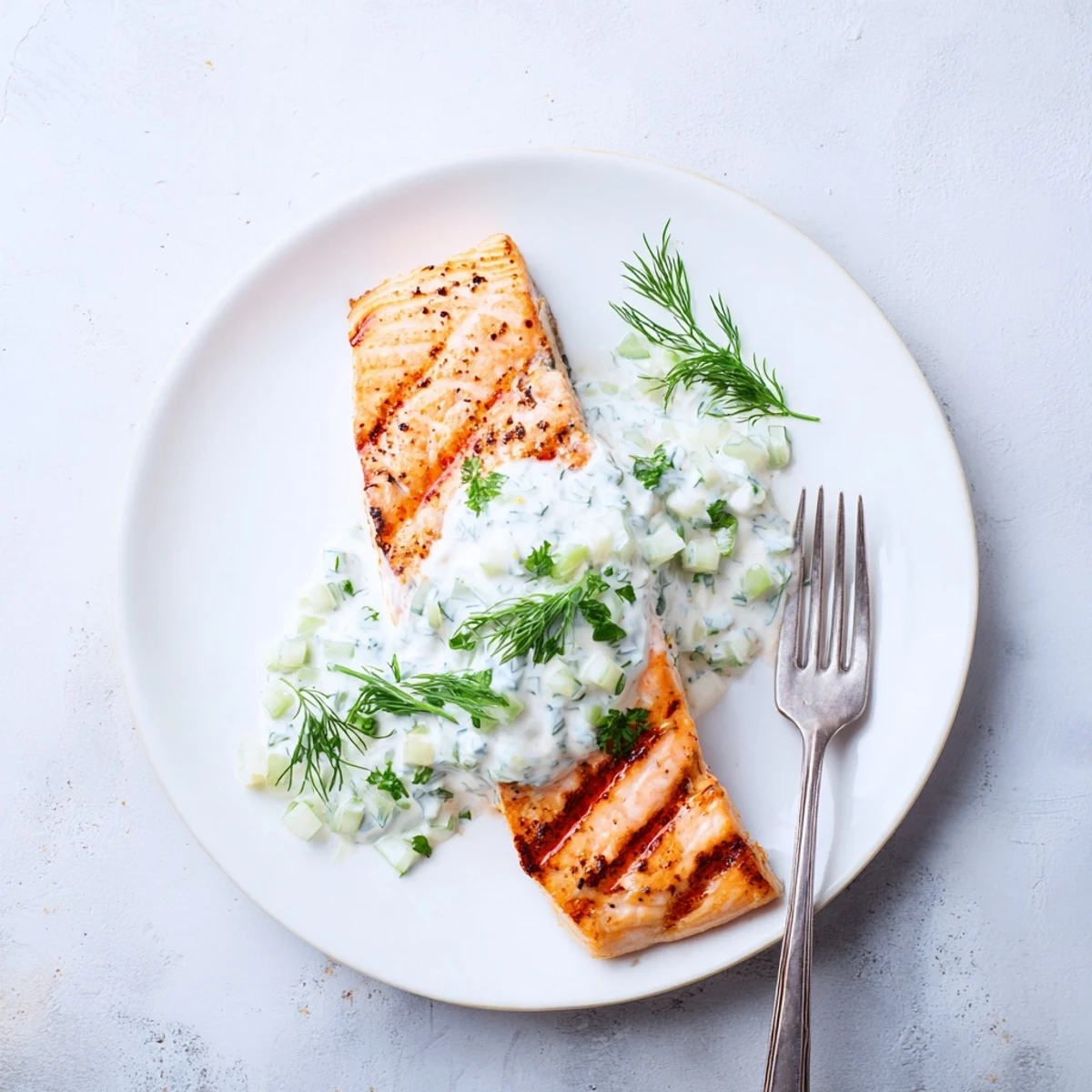 Fresh herb marinated salmon plated with tangy yogurt cucumber sauce and lemon wedges
