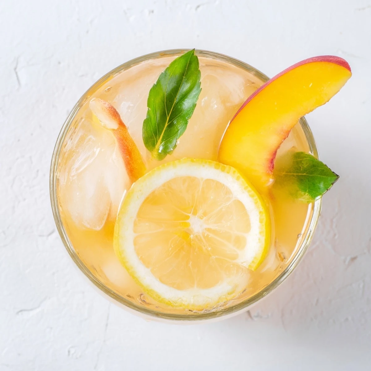 Golden fresh peach lemonade served in a glass with ice and peach slices